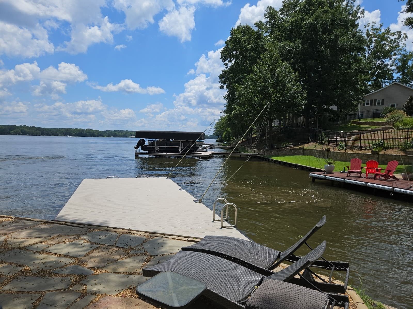 Waterfront view with dock, lounge chairs, and boat house under a bright blue sky.