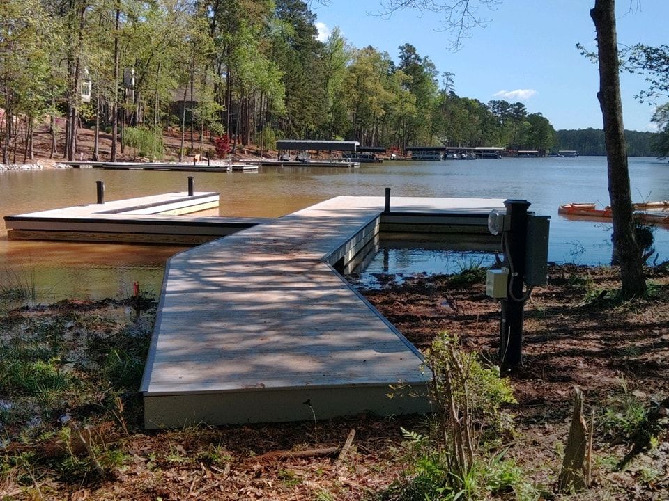 Dock extending into a lake, surrounded by shoreline and trees on a sunny day.