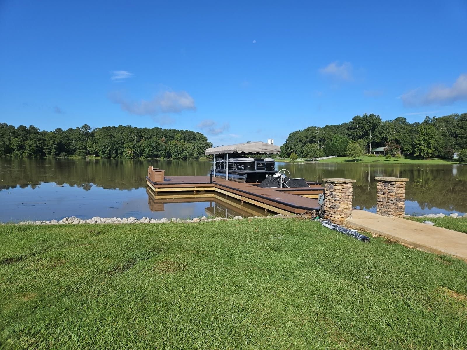 Dock extending into a calm lake with trees in background and clear blue sky.