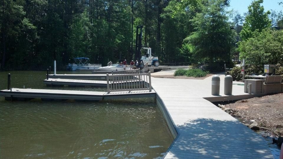 Dock with boats in a lake, concrete ramp leads to piers. Trees in the background, sunny day.