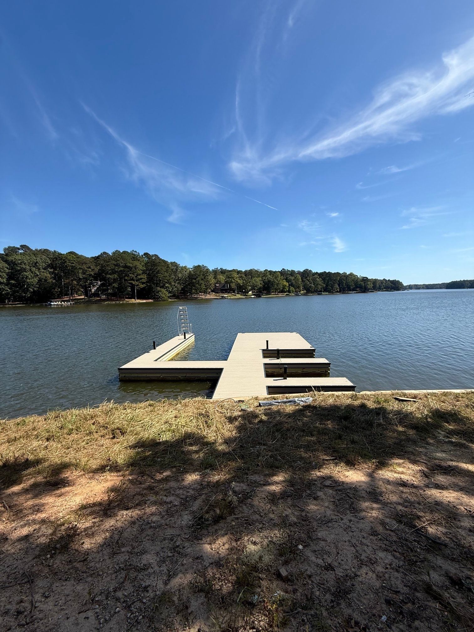 Dock extending into calm lake, blue sky with wispy clouds, trees on the distant shore.