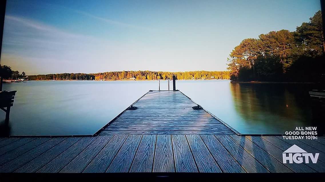 Wooden dock extends into a calm lake, trees in the background, blue sky, HGTV logo in the corner.