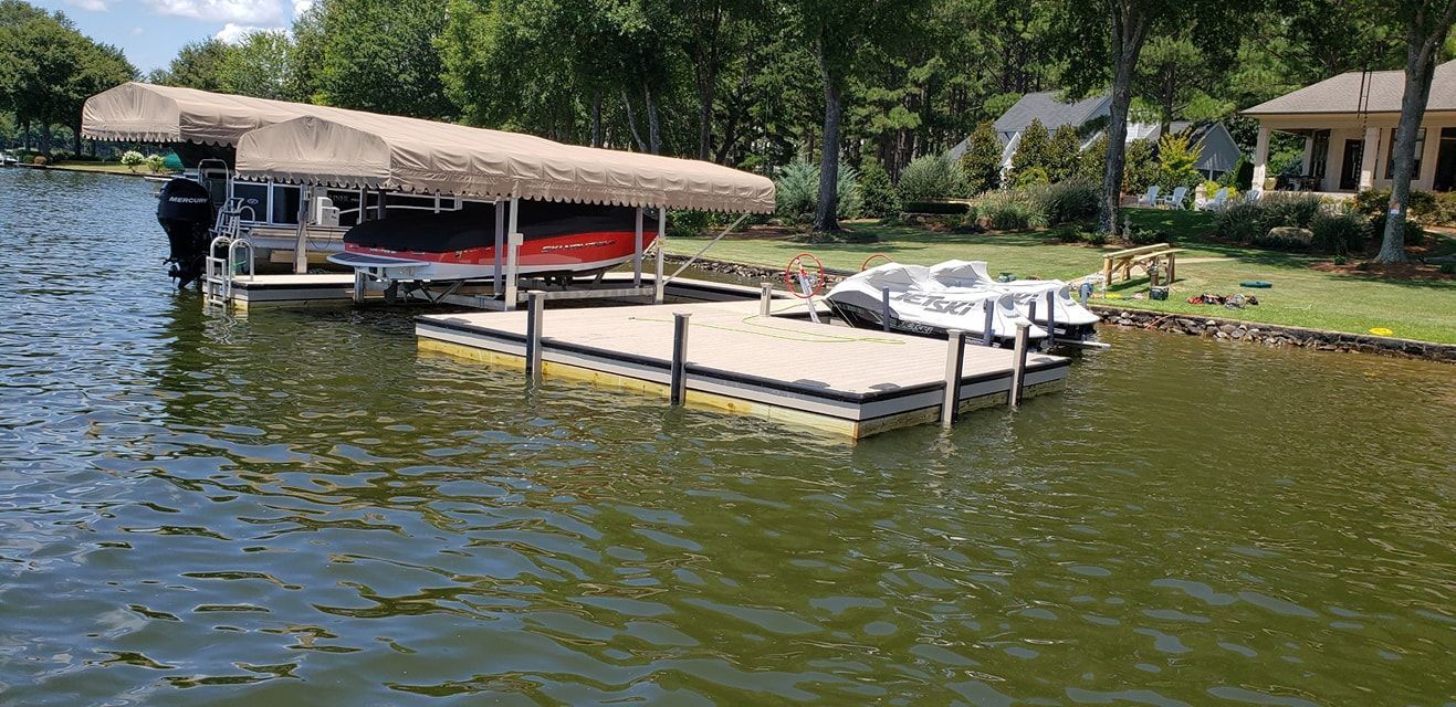 Boats docked at a lake dock with a red boat cover, grass, and trees.