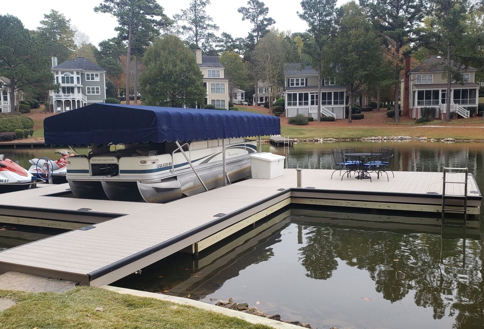 Dock with a covered pontoon boat on a lake. Houses in the background.