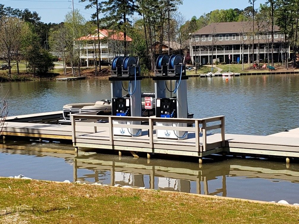 Fuel pumps on a dock in a lake with houses in the background.