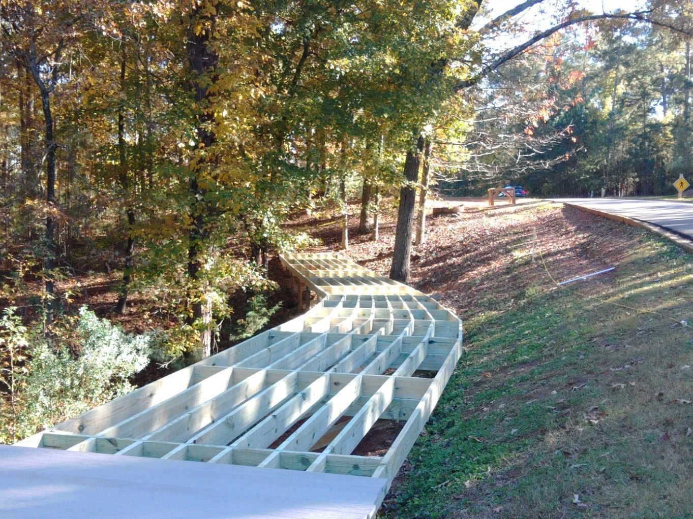 Wooden deck frame being built along a roadside, in a wooded area with trees.