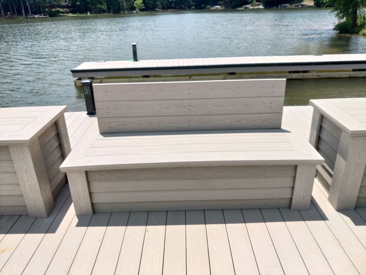 Outdoor seating on a wooden dock overlooking a lake. Bench and two side tables are light gray.