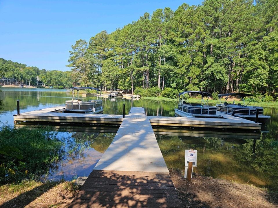 Dock on a lake with pontoon boats, surrounded by green trees under a blue sky.