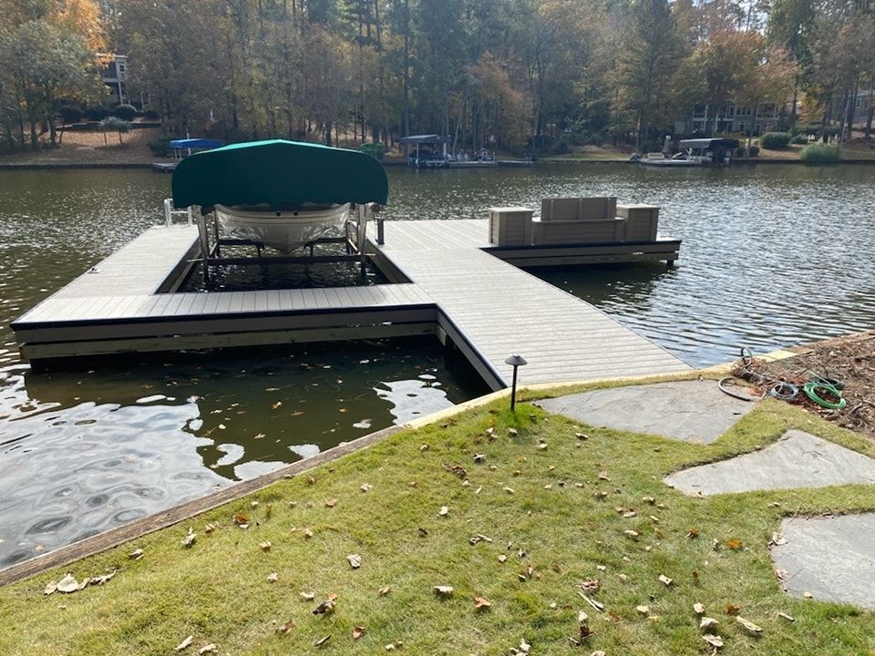 Dock on a lake with a covered boat lift and a seating area. Green lawn in the foreground; trees in the background.