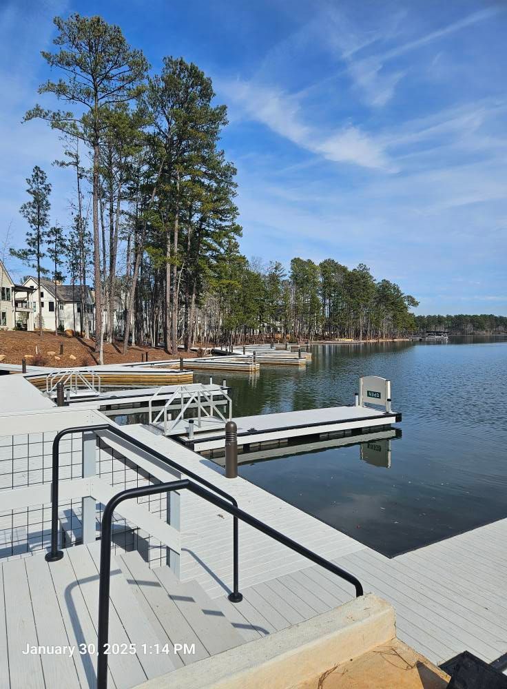 Dock on a lake with white platforms, handrails, and surrounding trees under a blue sky.