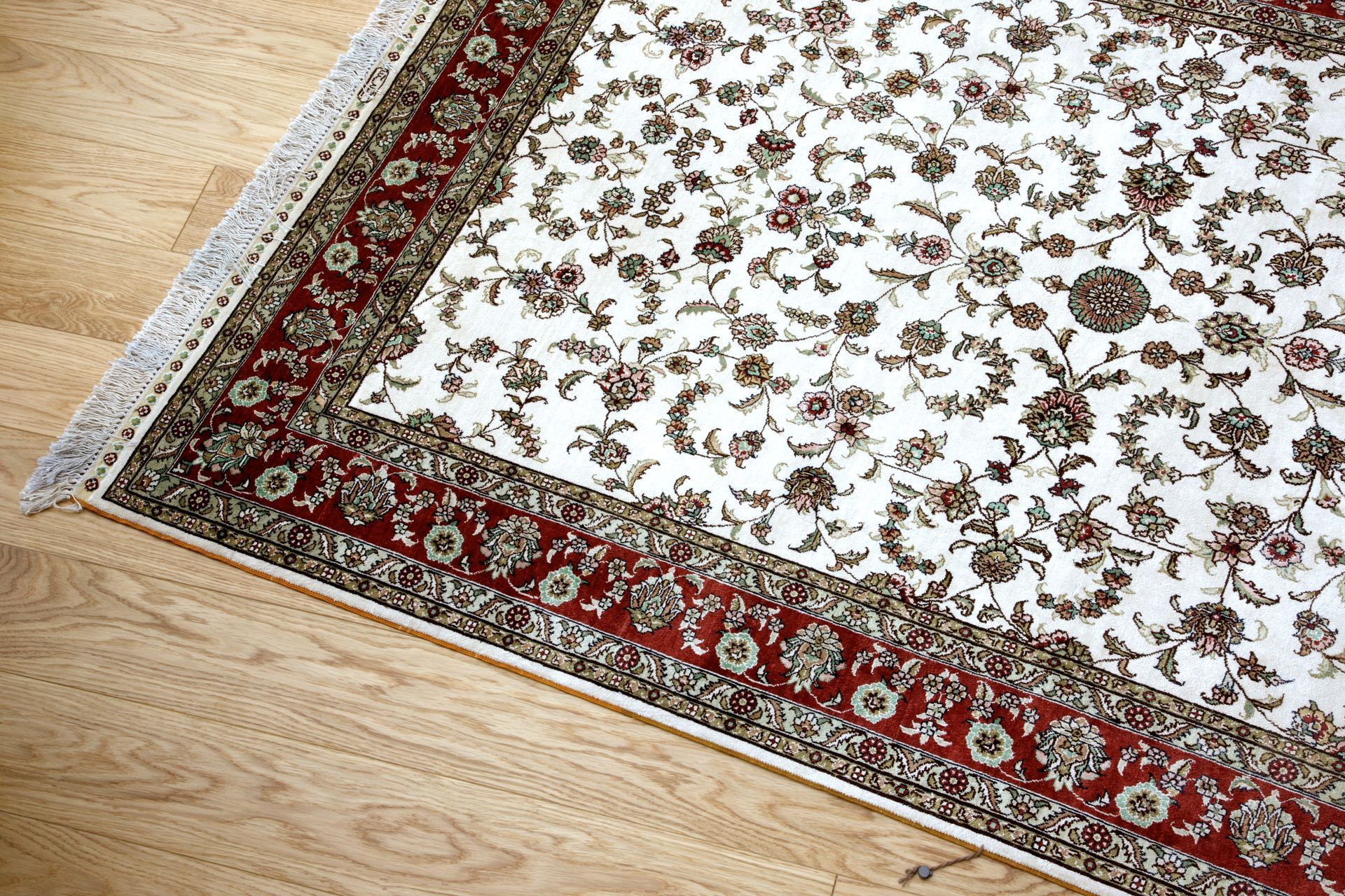 Corner of a cream and red patterned rug on a light wood floor