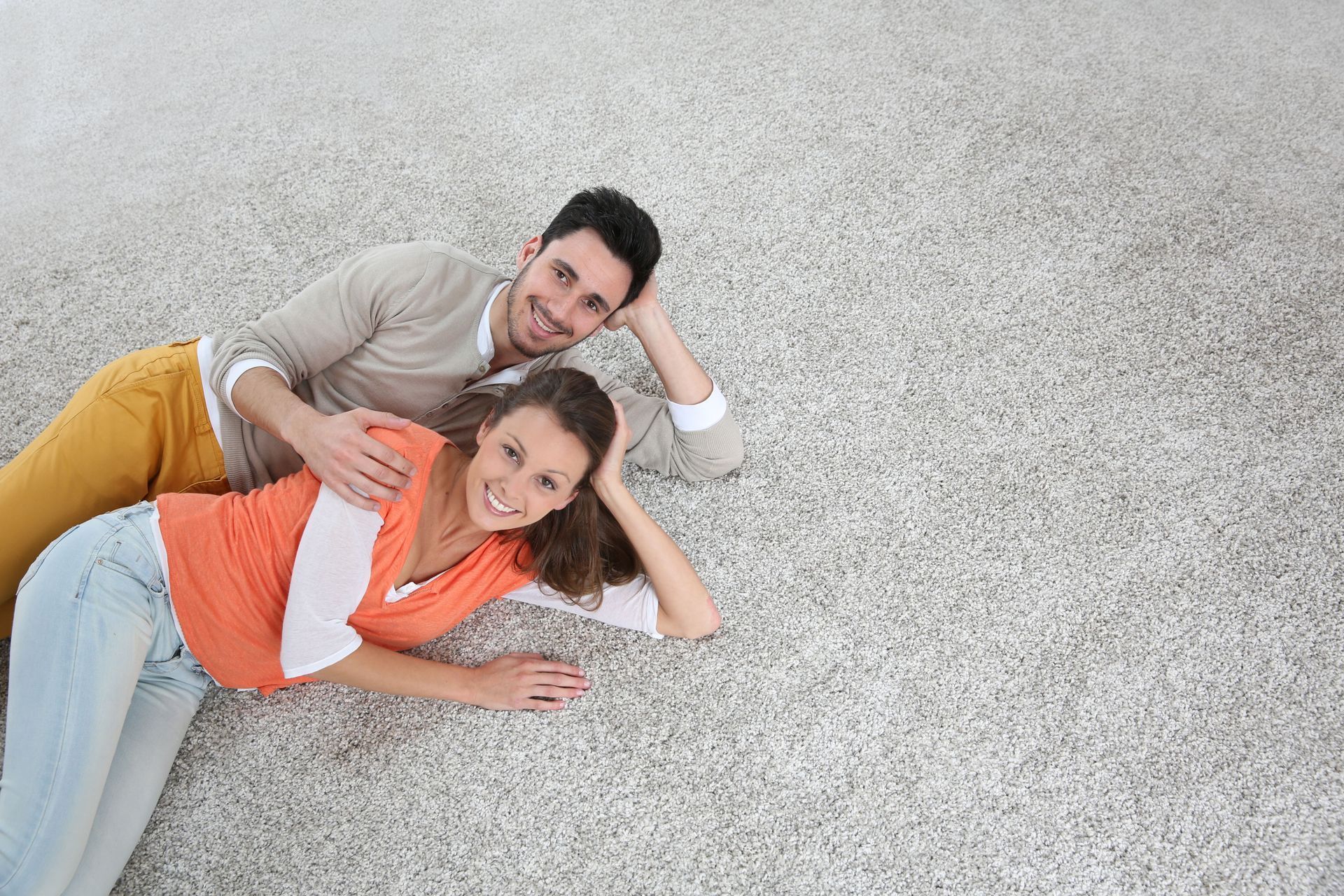 Couple lying on the floor, smiling with heads resting on their hands.