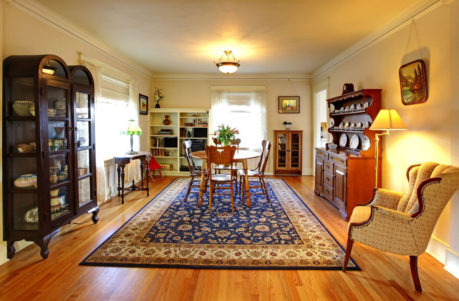 Bright dining room with a blue rug, wooden table and chairs, cabinets, and warm lamplight