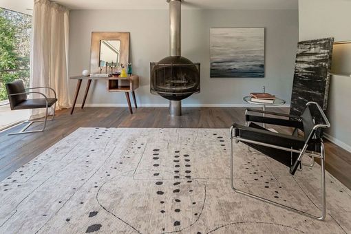 Modern living room with a large patterned rug, hanging chair, desk, and abstract wall art.