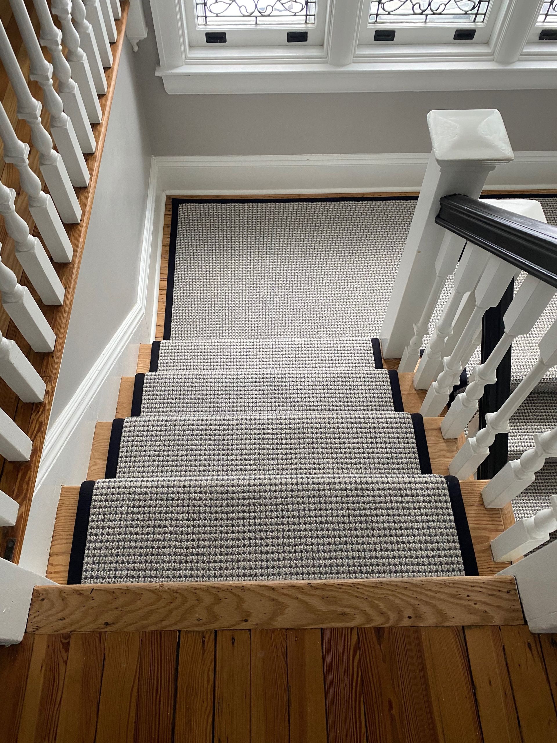 Carpeted staircase viewed from the top, with white railings and wooden floor at the landing.