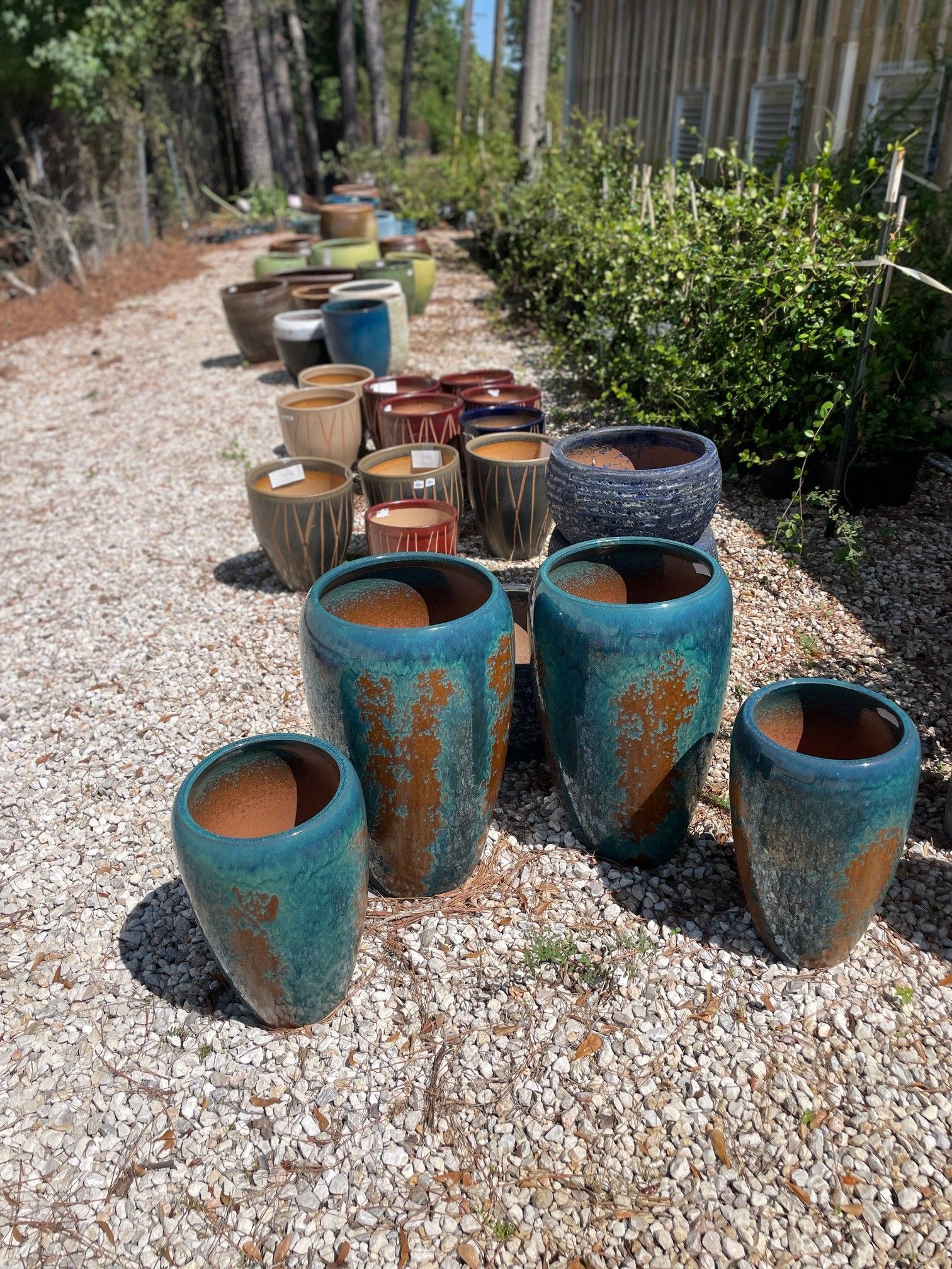 Row of ceramic pots in various colors and sizes on a gravel path outside a garden center.