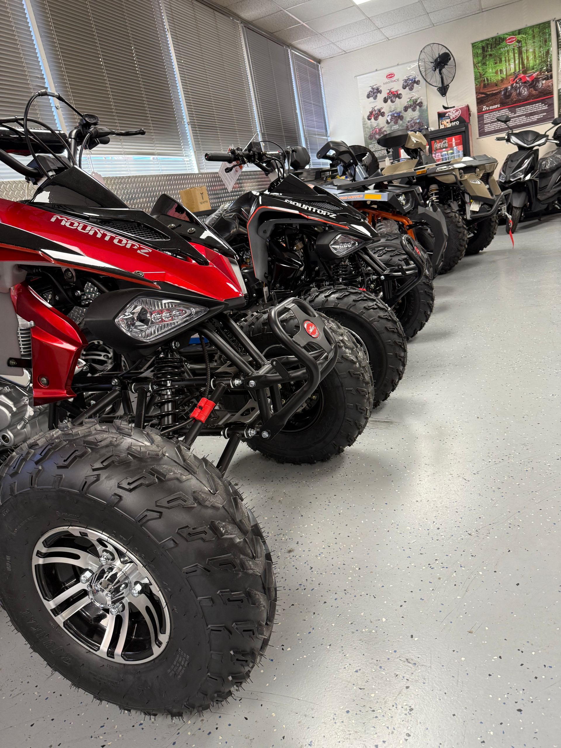 ATVs lined up indoors, including a red one in the foreground with large off-road tires.