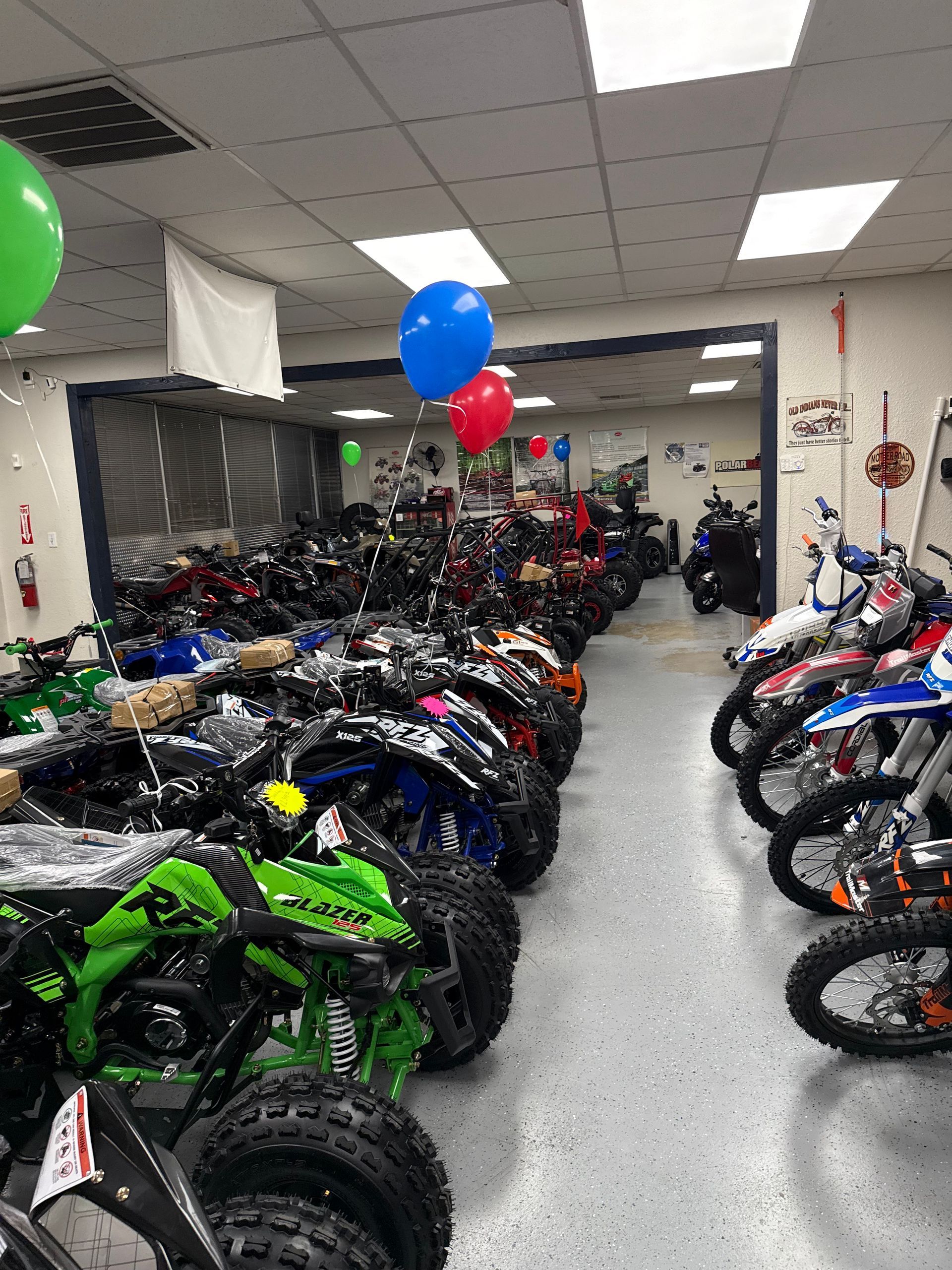 Rows of ATVs and dirt bikes in a showroom with balloons hanging from the ceiling