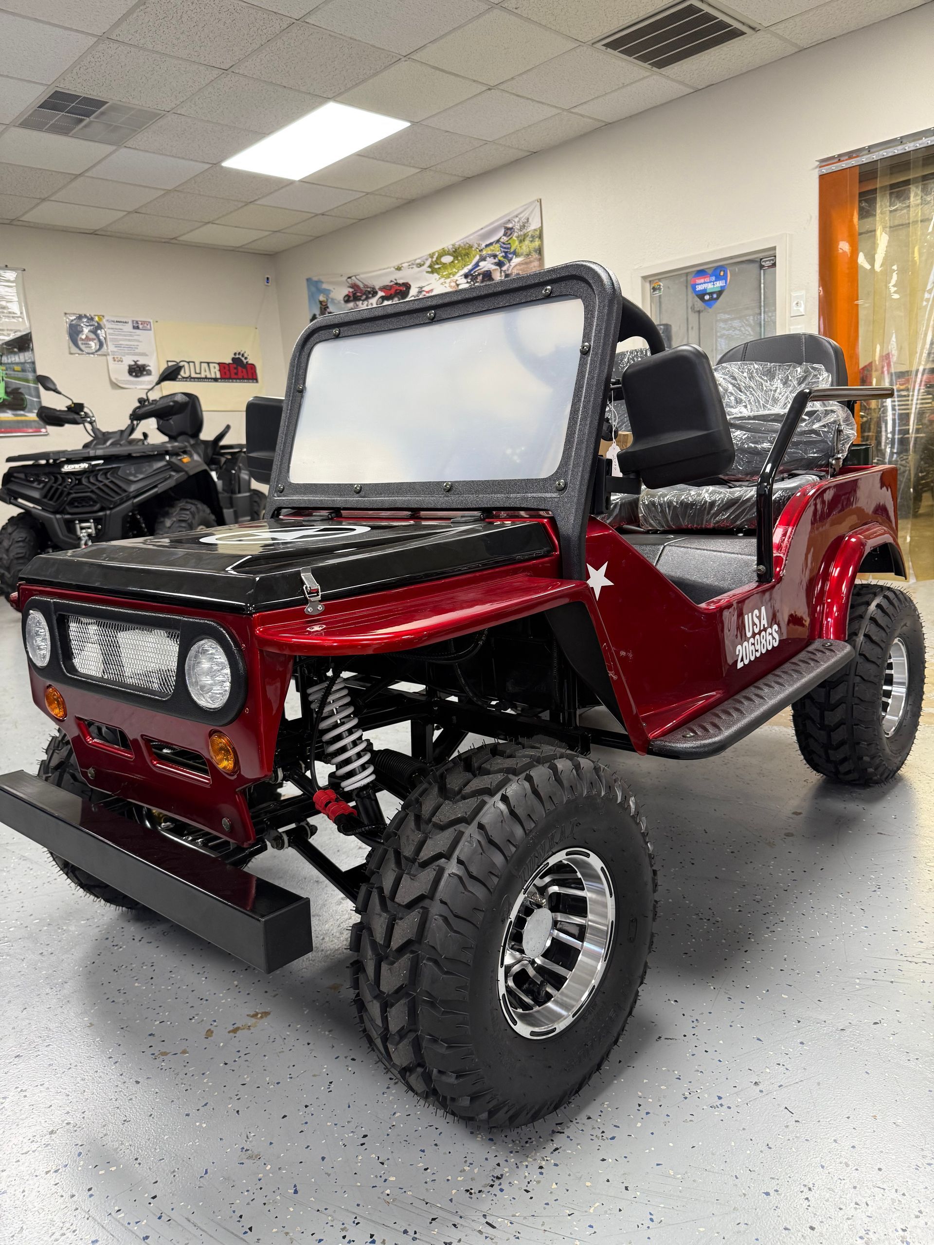 Red off-road buggy with large tires in a showroom, viewed from the front-left.