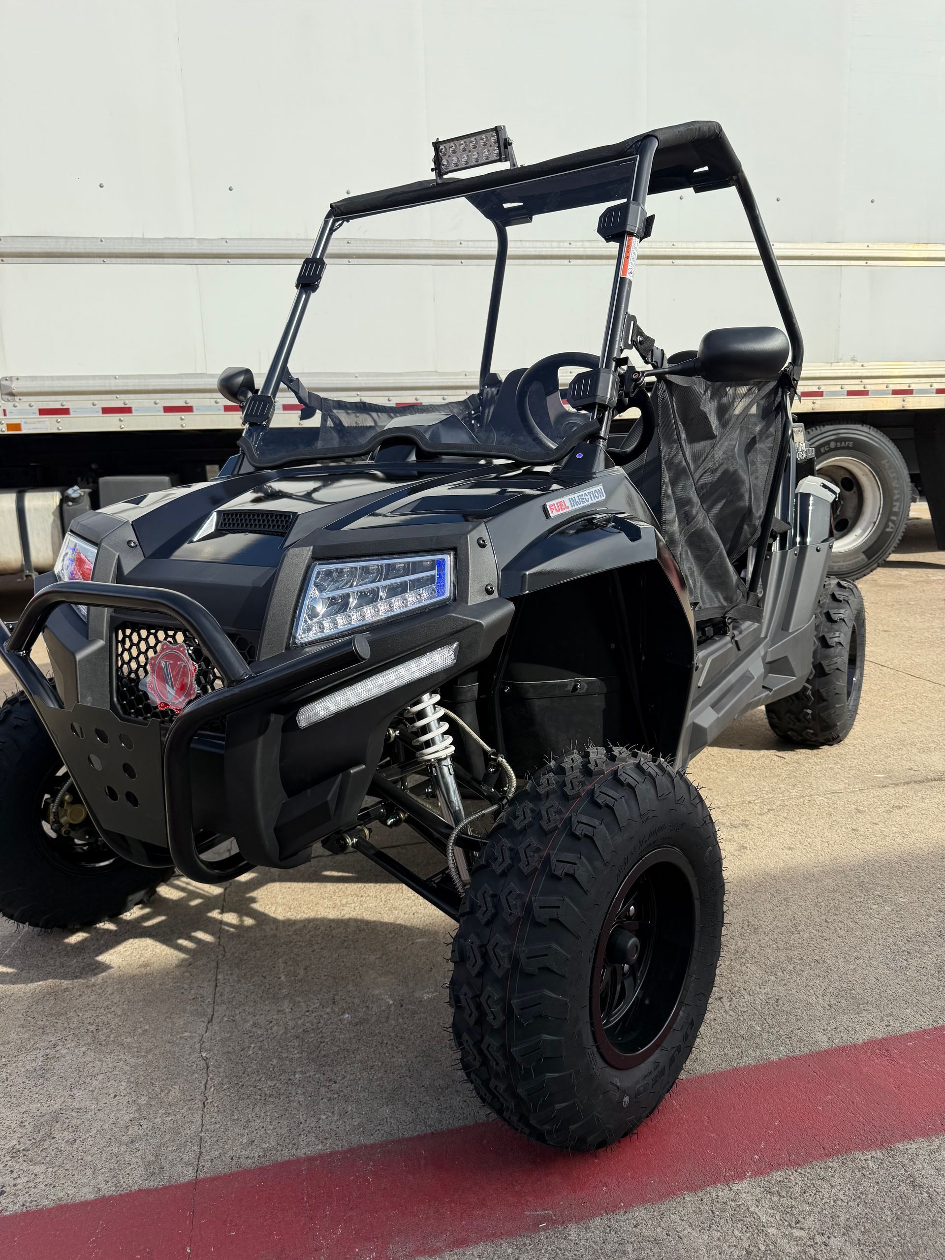 Black off-road UTV parked outdoors on pavement, with roll cage and large knobby tires