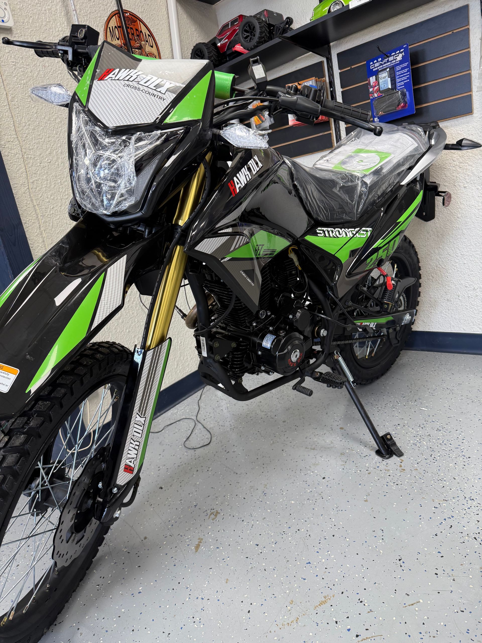 Black and green dirt bike parked indoors on a garage floor with a stand and visible front plate