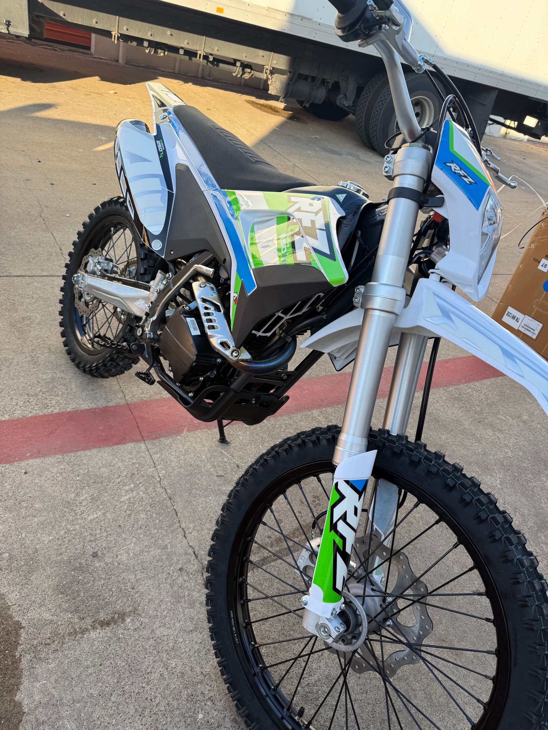Blue and green dirt bike parked on a sidewalk near cardboard boxes