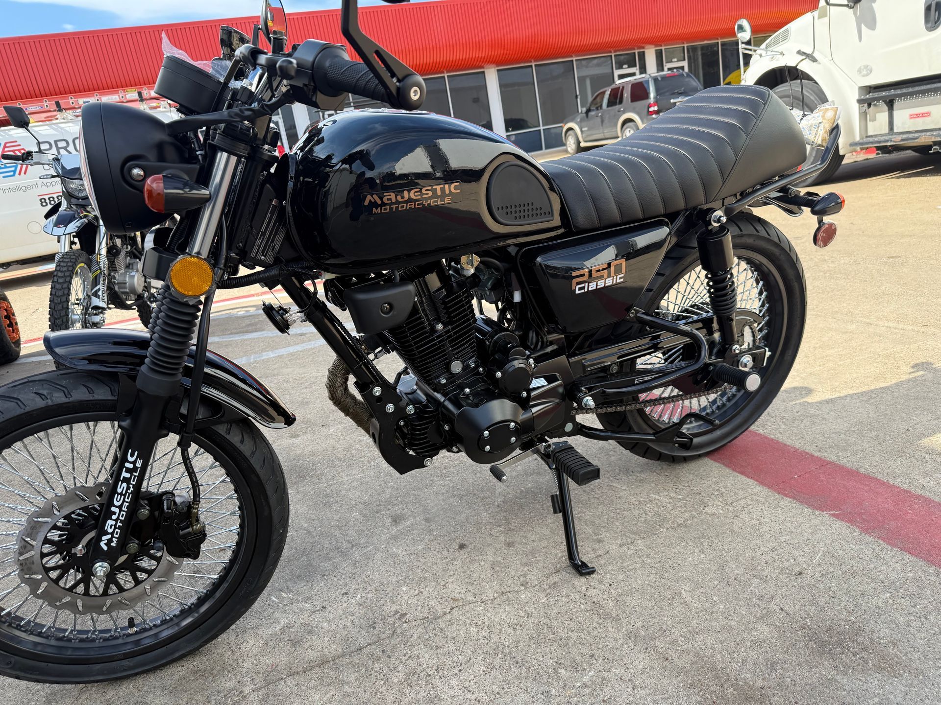 Black motorcycle with a stitched seat parked on pavement at a gas station, side view
