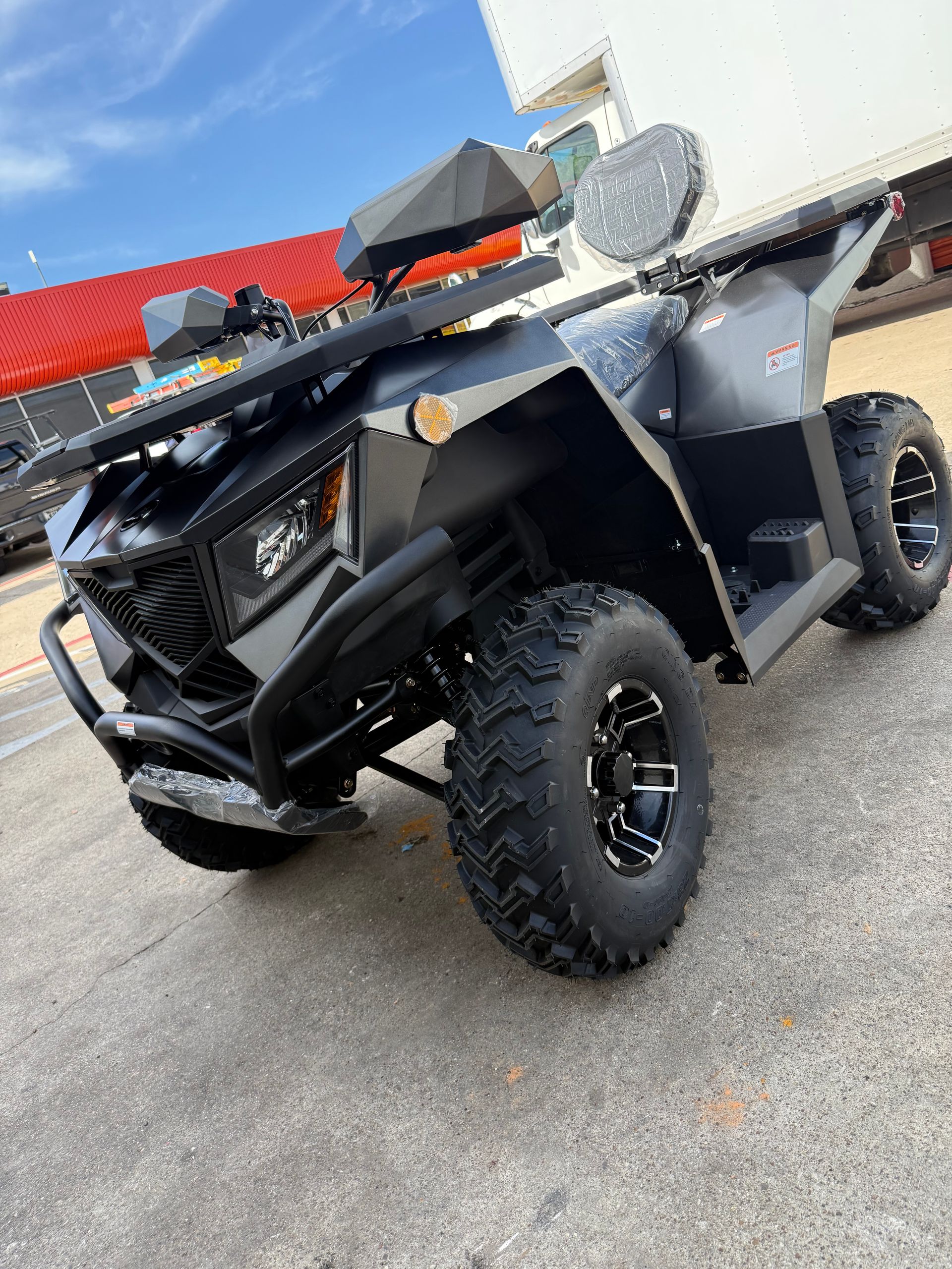 Black off-road ATV parked outdoors, angled front view with large knobby tires and gray body panels.