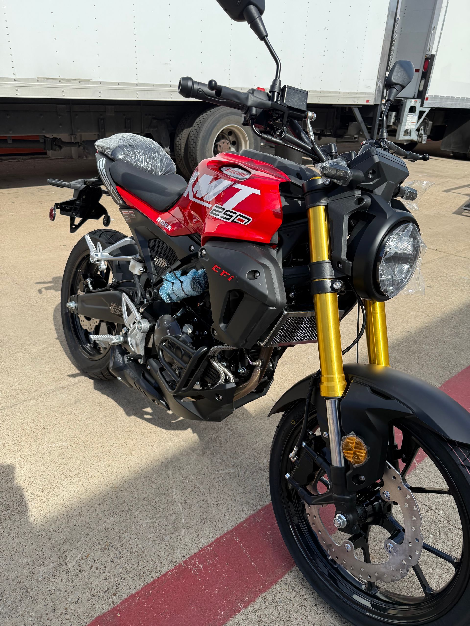 Red and black motorcycle with gold front forks parked on a concrete lot.