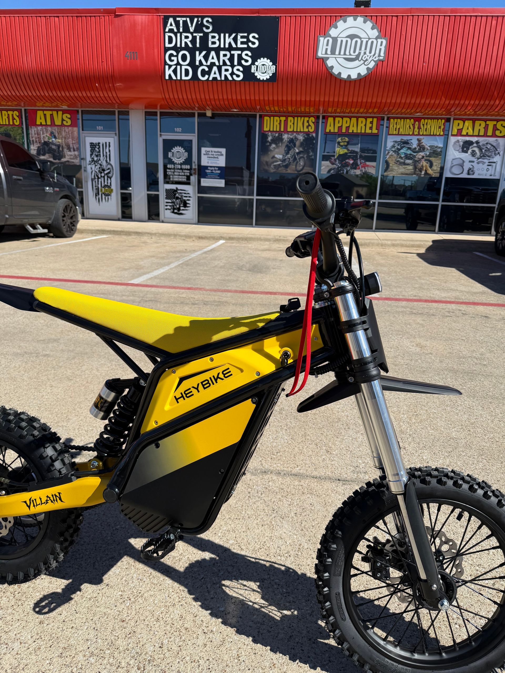 Yellow and black dirt bike parked outside a motorcycle shop with red awning and gear signs.