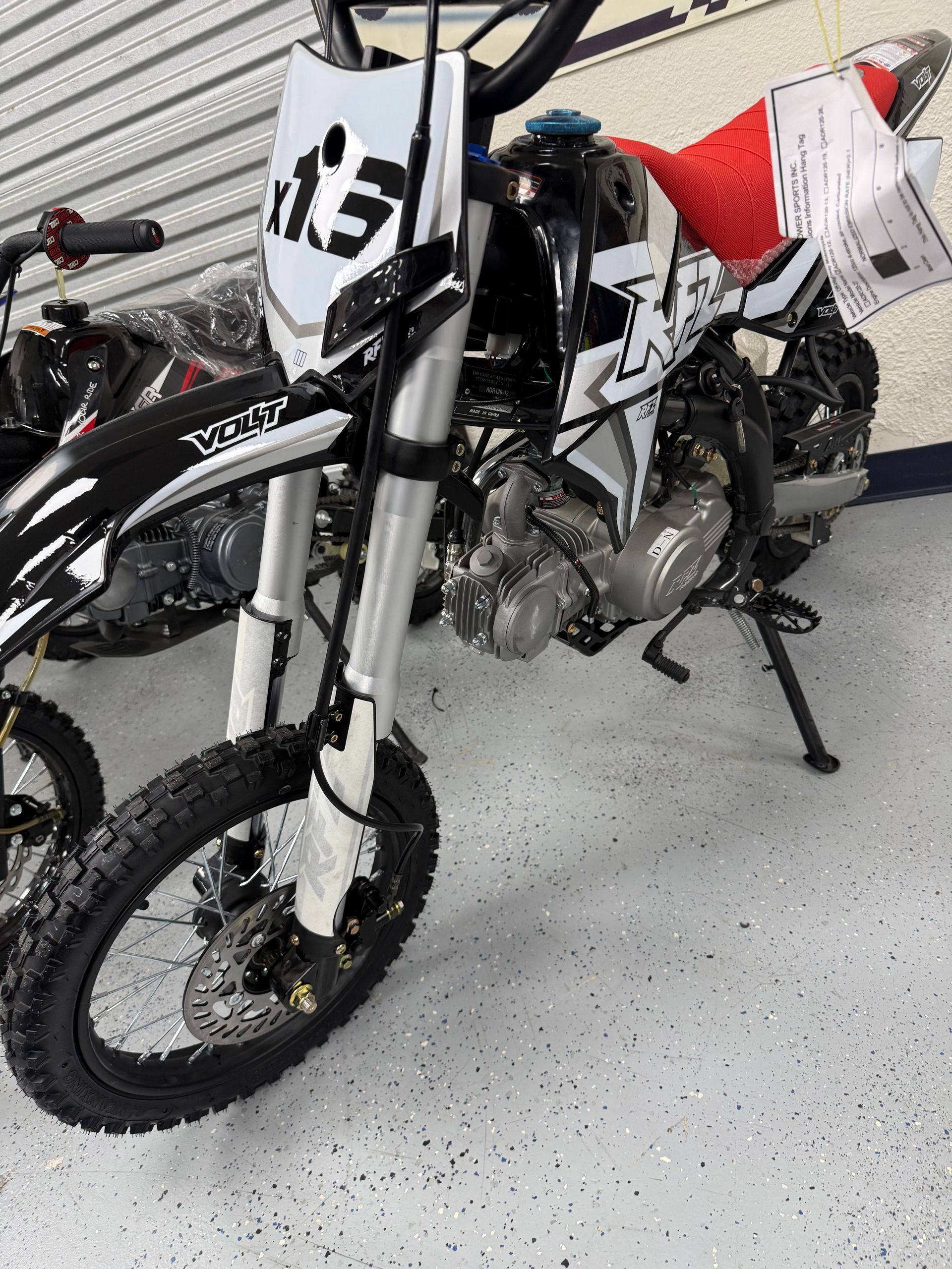 White dirt bike with black graphics in a showroom, shown from the front-left side.