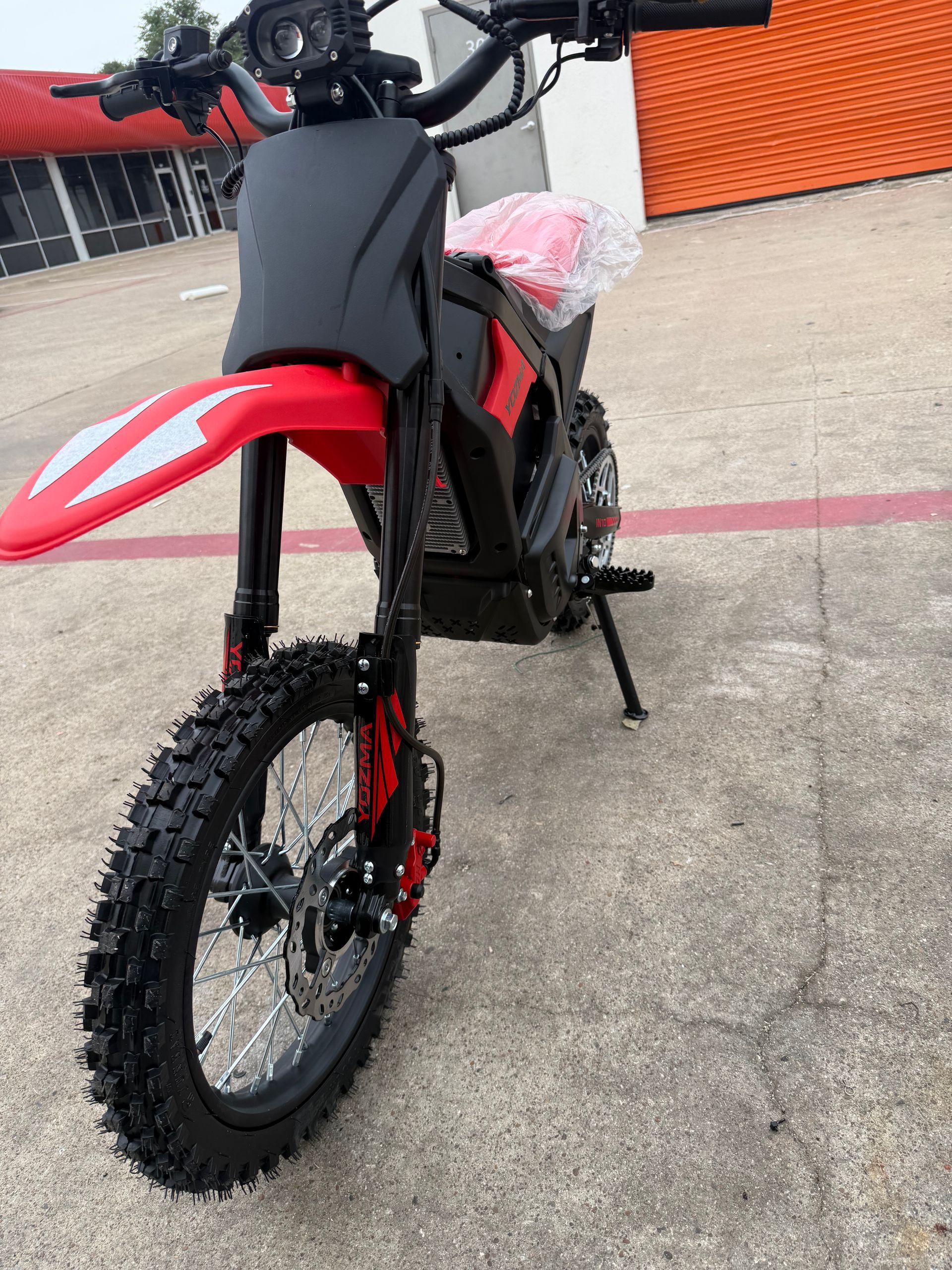 Red dirt bike parked on concrete, front view with black frame and red fenders.