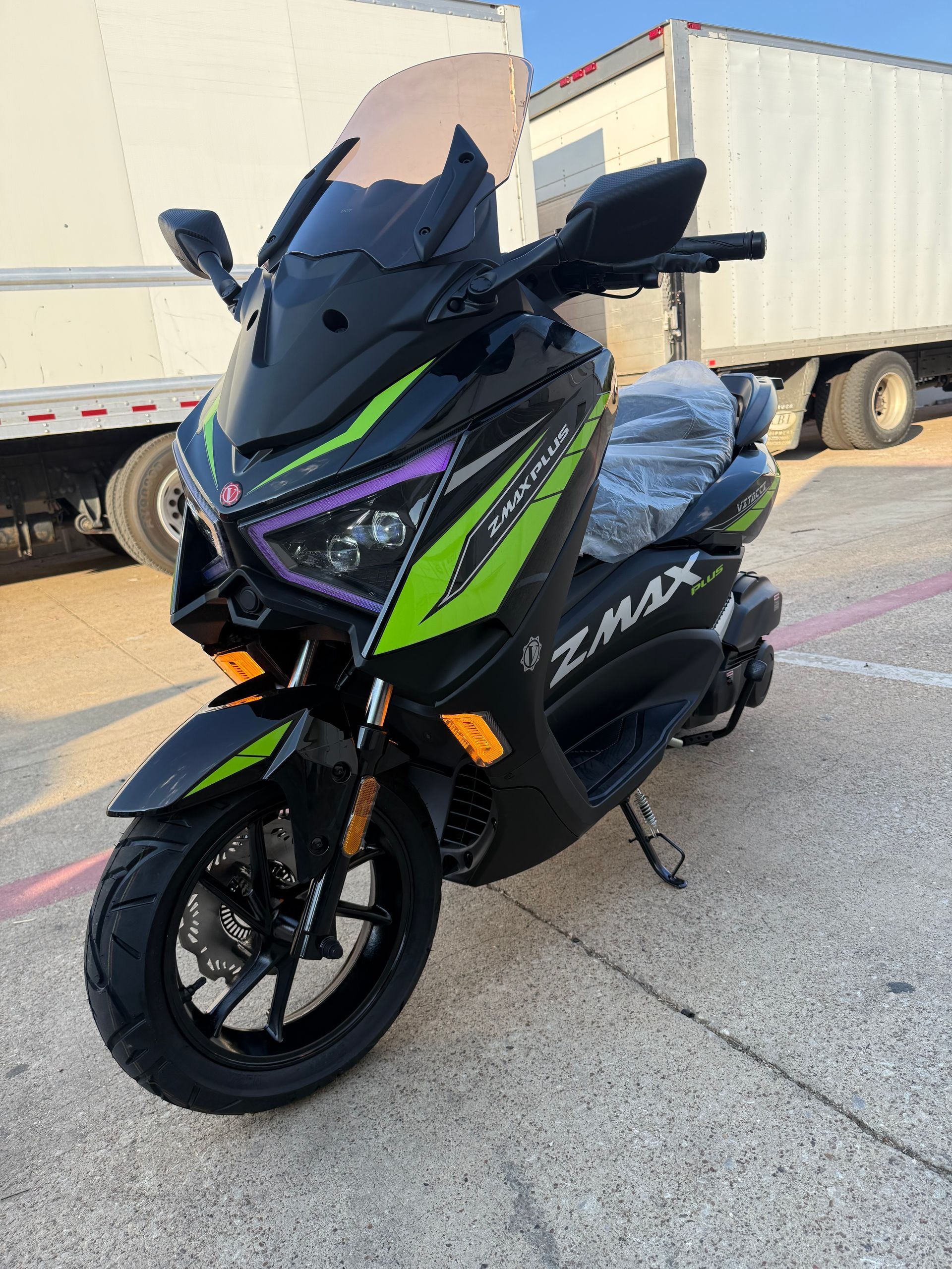 Black and neon green sport scooter parked beside white semi-trucks on pavement