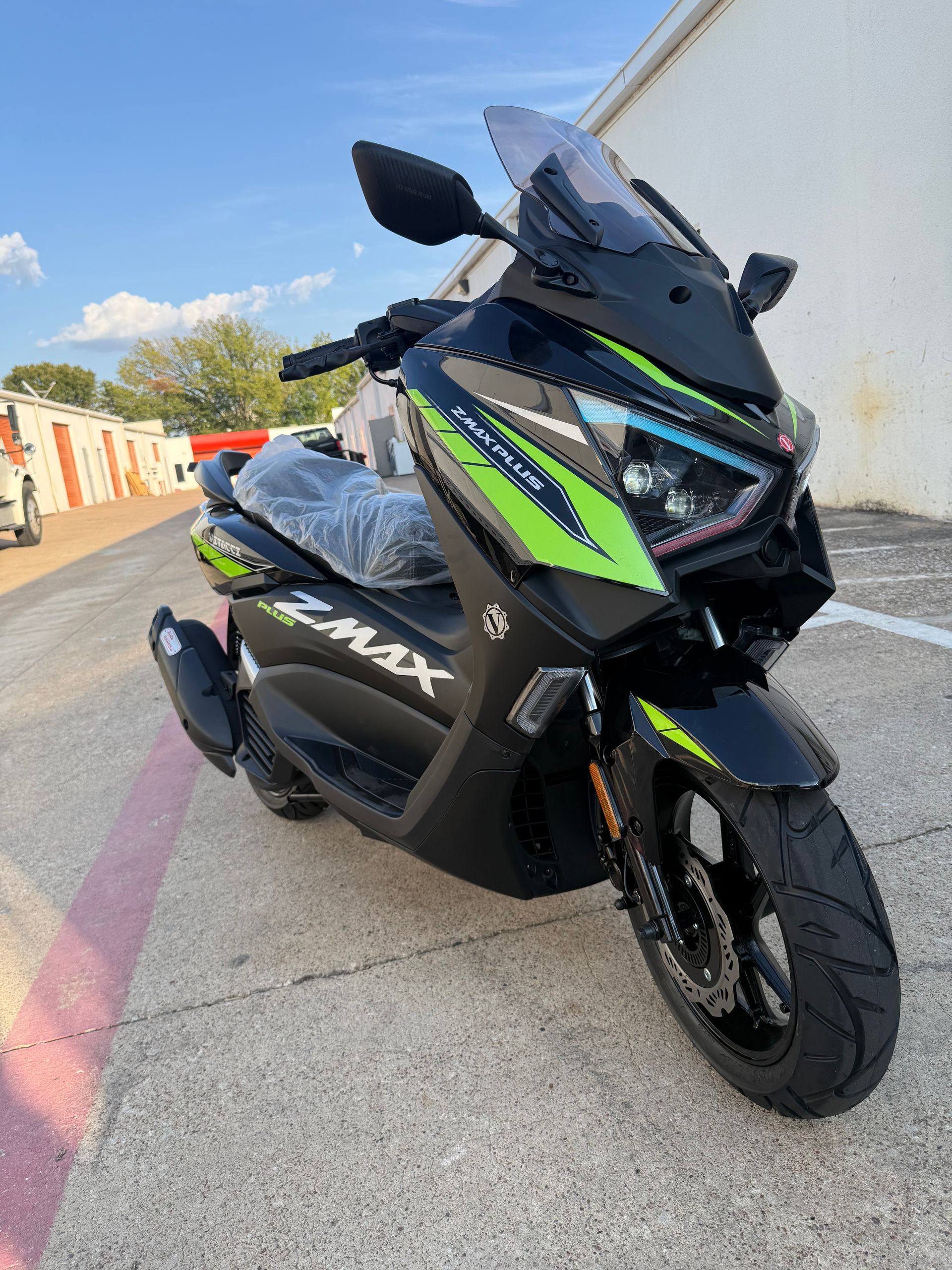 Black and green maxi-scooter parked on a sunlit street, angled front view.