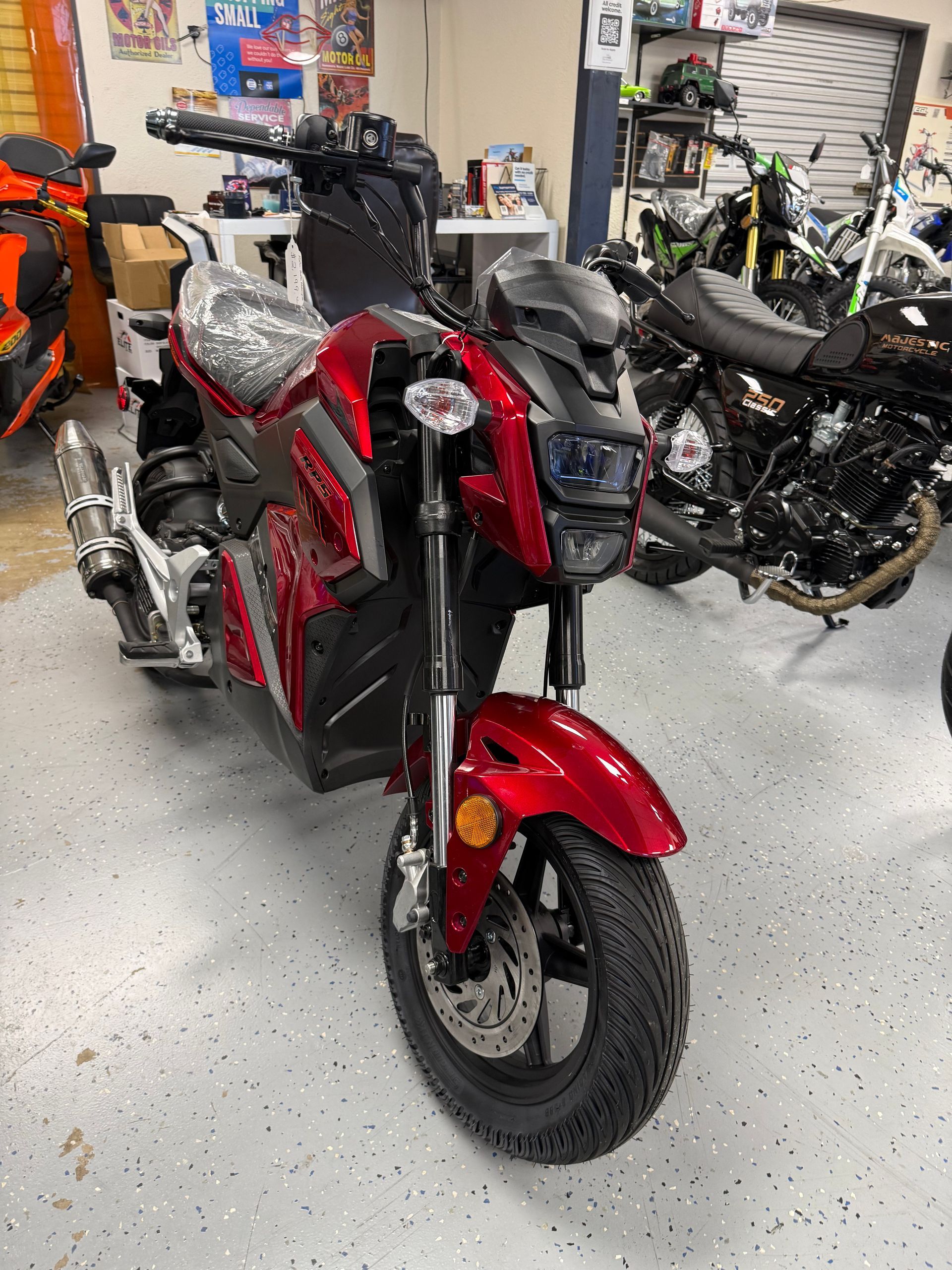 Red motorcycle parked indoors in a garage beside several other bikes and tools.