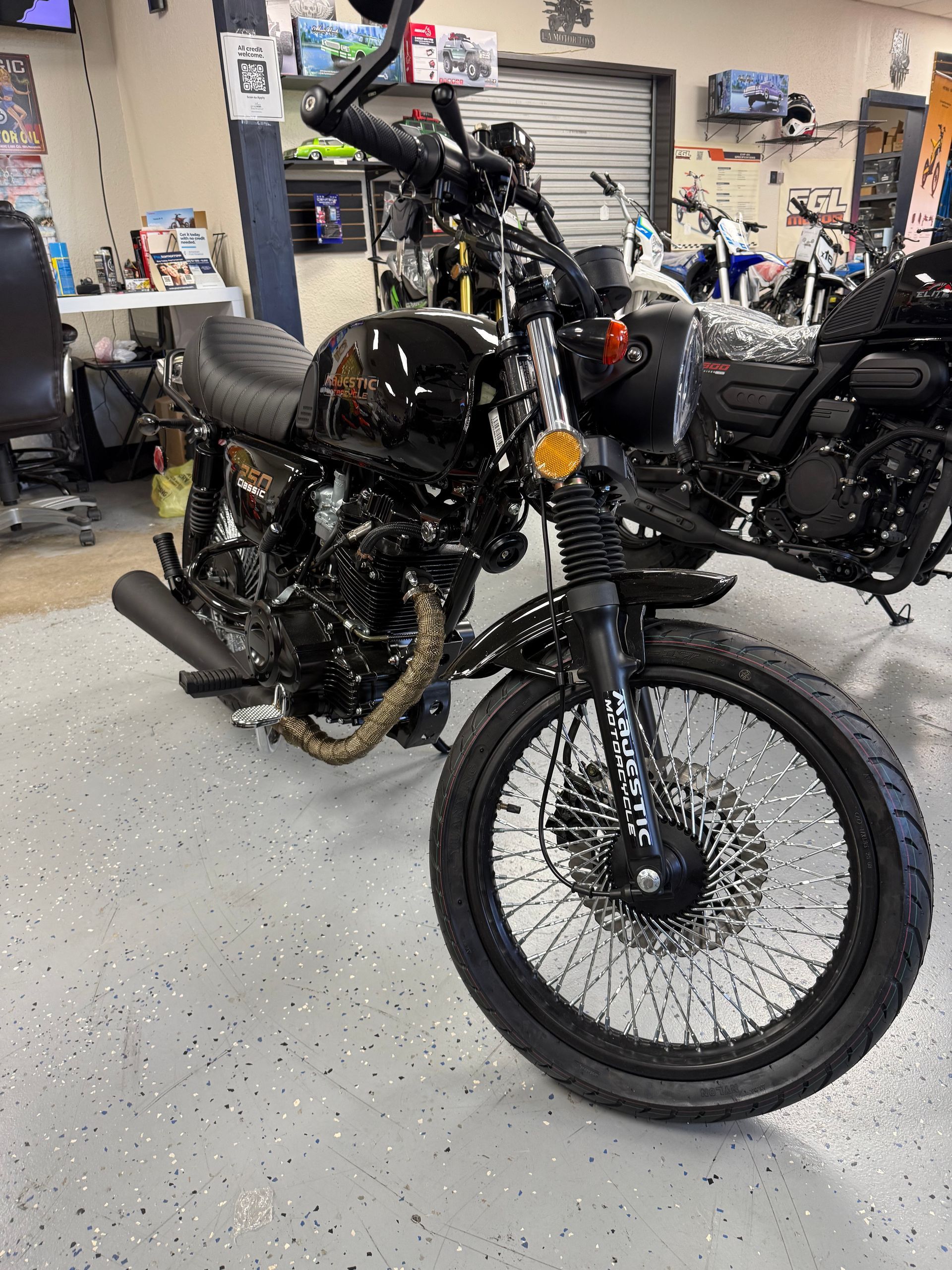 Black custom motorcycle with high front wheel in a garage workshop, surrounded by other bikes.