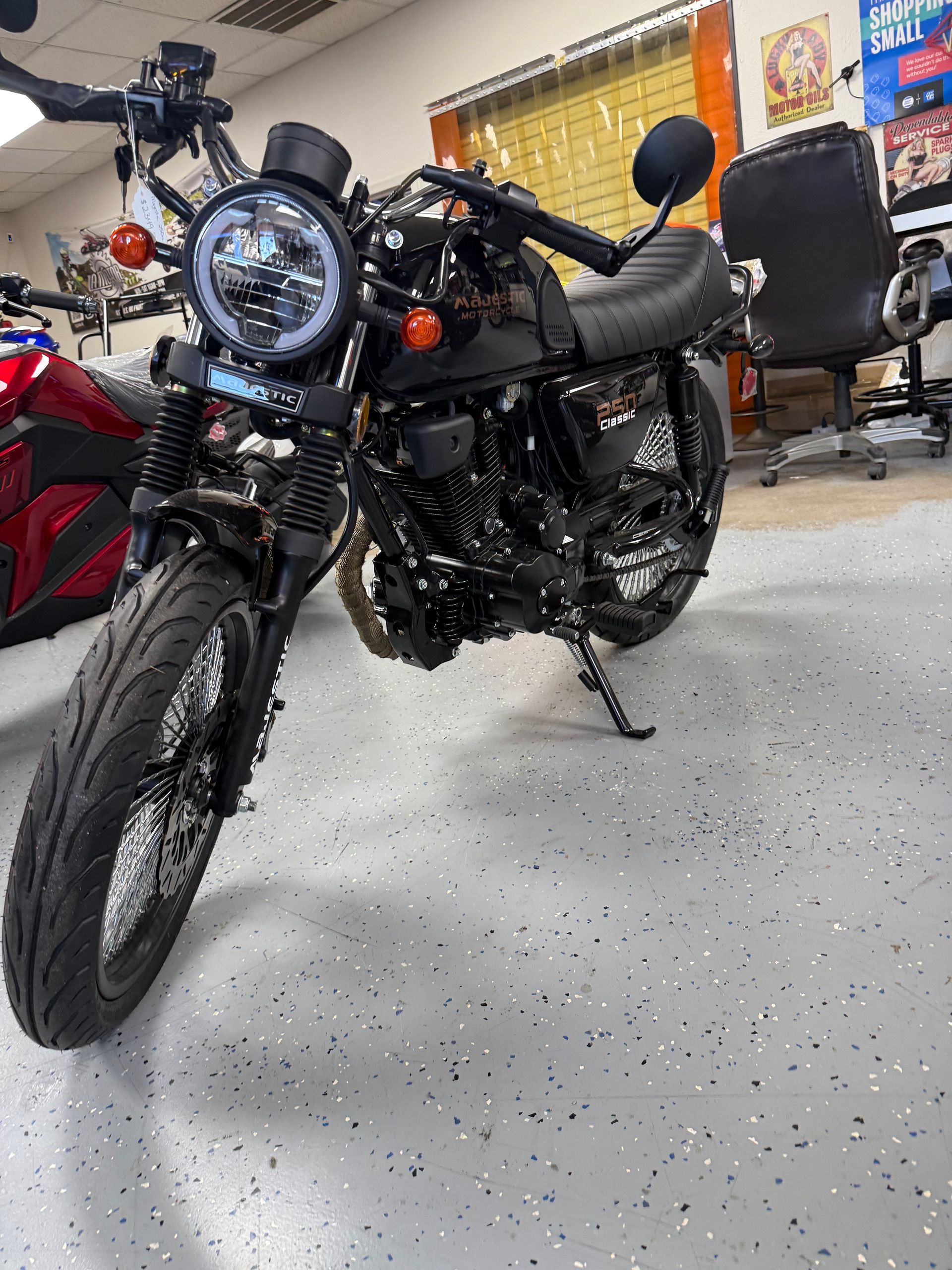Black motorcycle with round headlight in a showroom garage, parked on a speckled floor.
