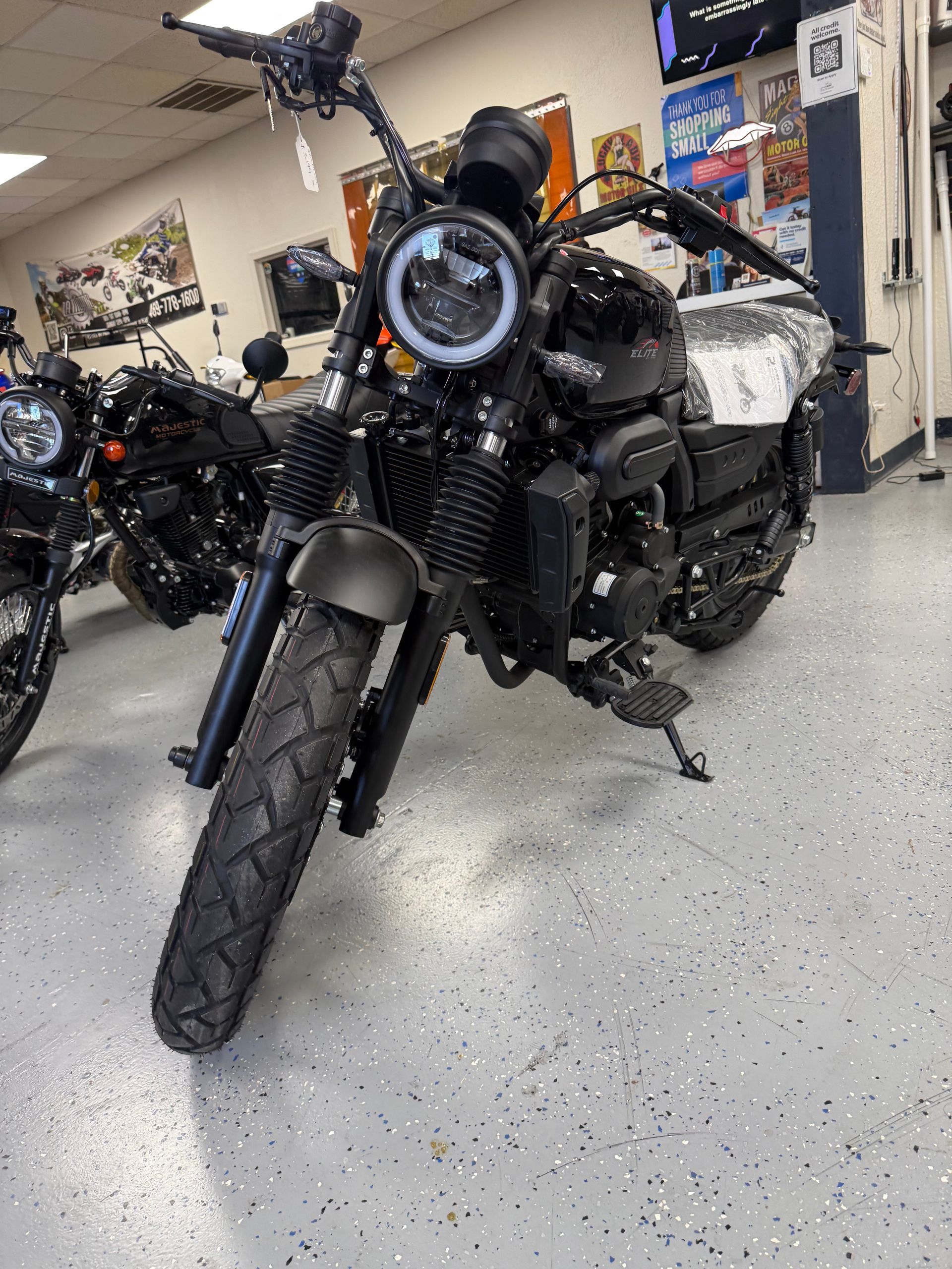 Black motorcycle with round headlight in a workshop, front view on a speckled floor.