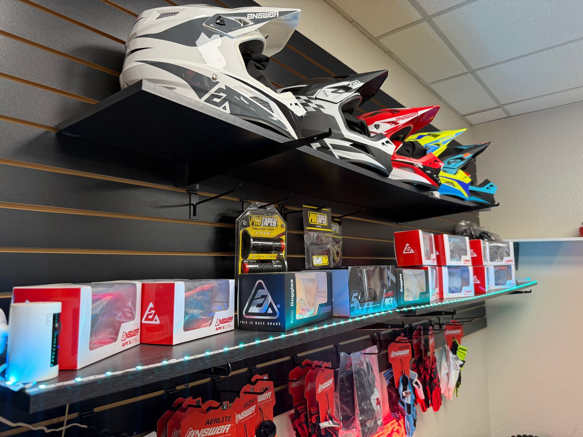 Shelf of motorcycle gear and accessories, with helmets on top and colorful boxes and gloves below.