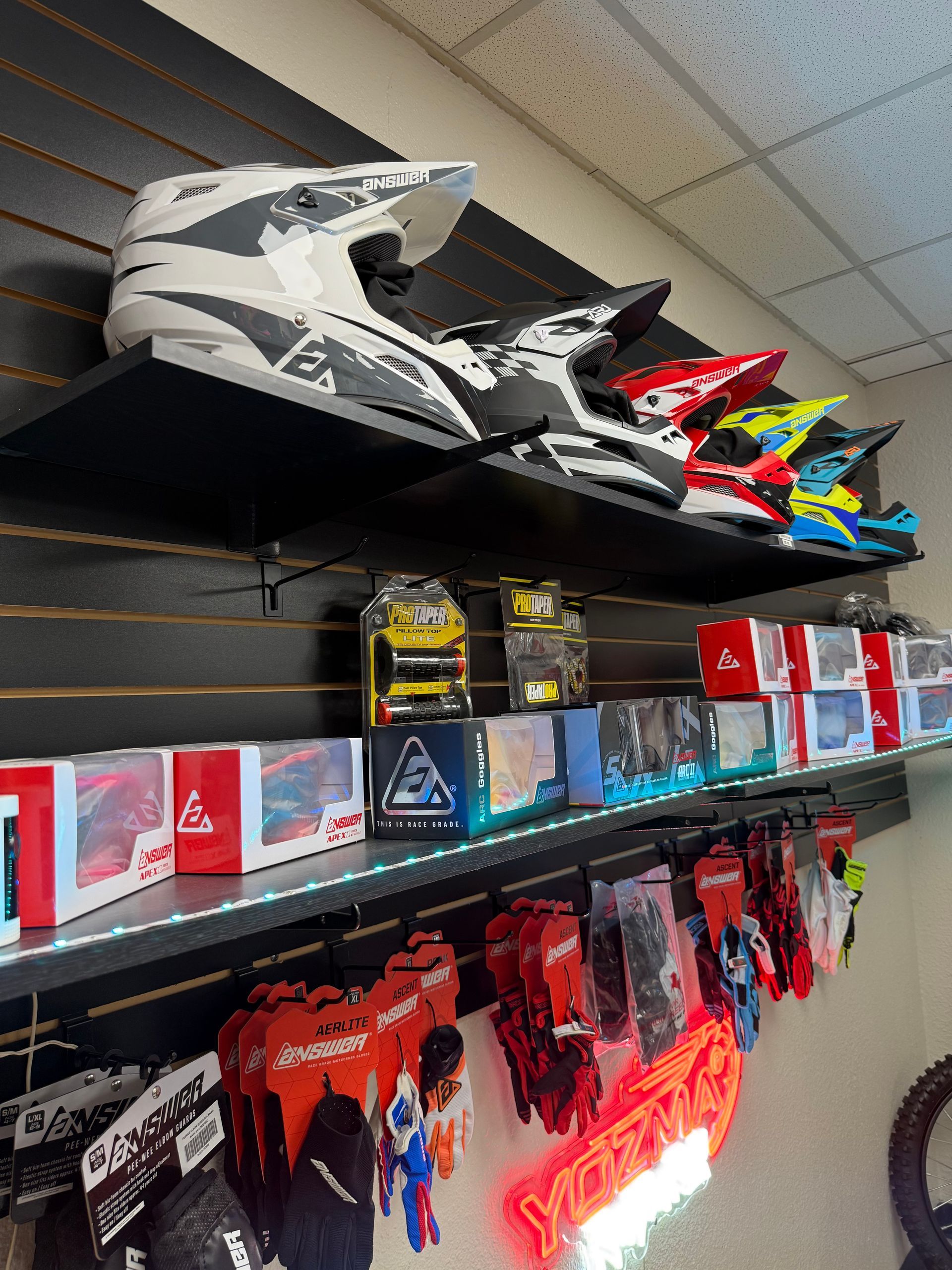 Store display of colorful racing-style helmets and boxed merchandise on shelves beneath a black-and-white helmet.