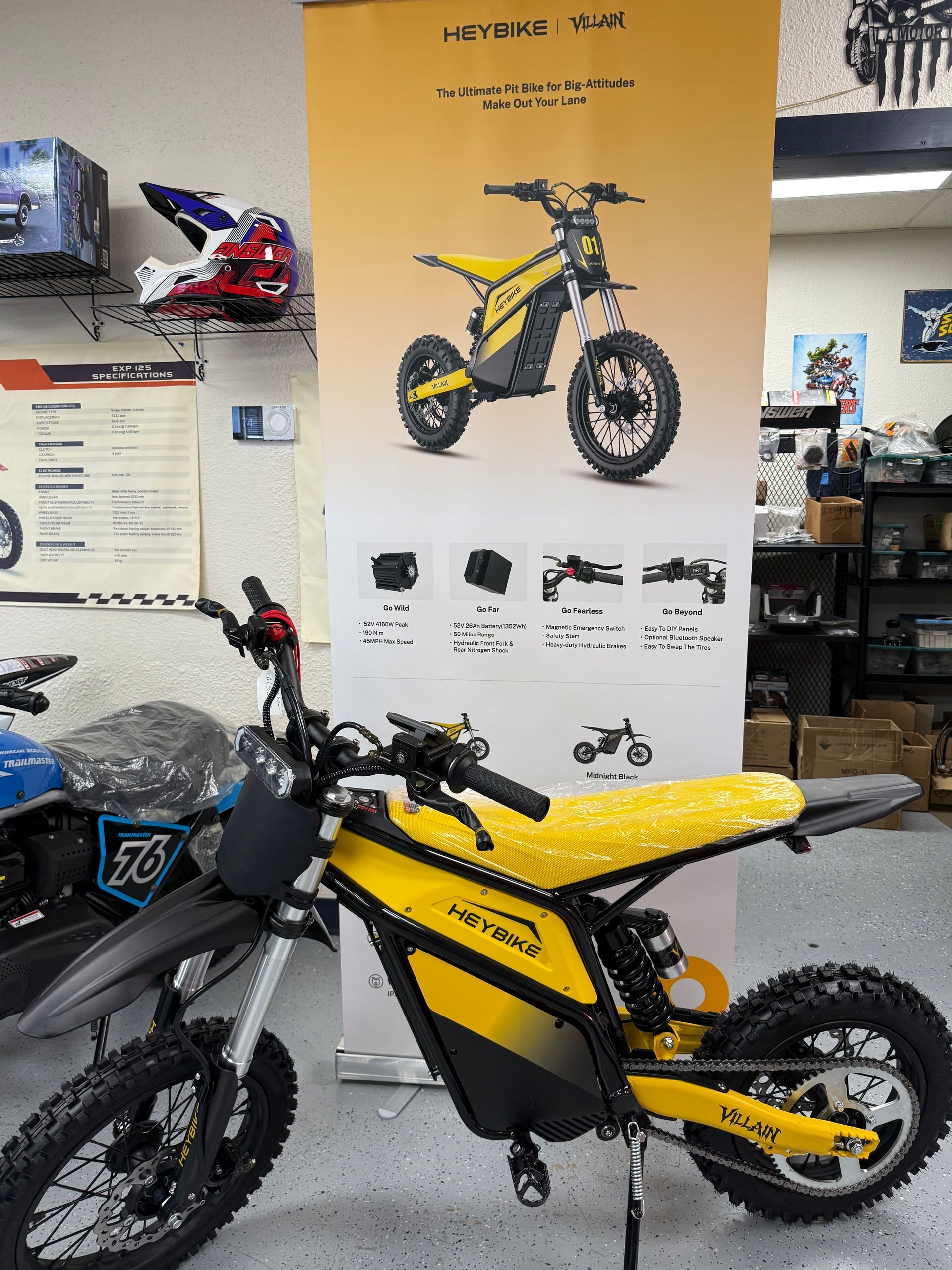 Yellow electric dirt bike displayed in a showroom, with posters of similar bikes on the wall.
