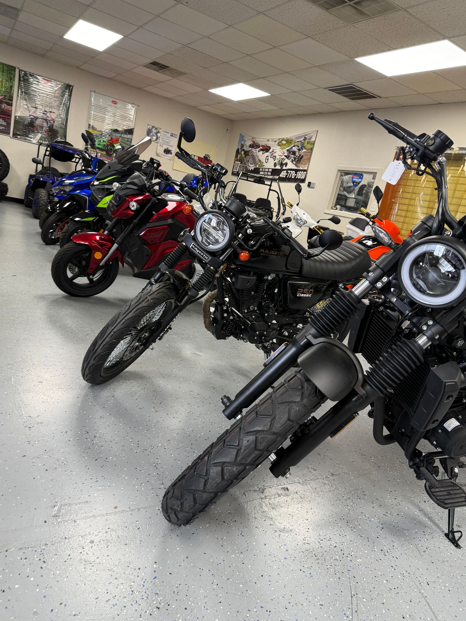 Motorcycles lined up in a showroom, including black, red, blue, and orange bikes on a polished floor.