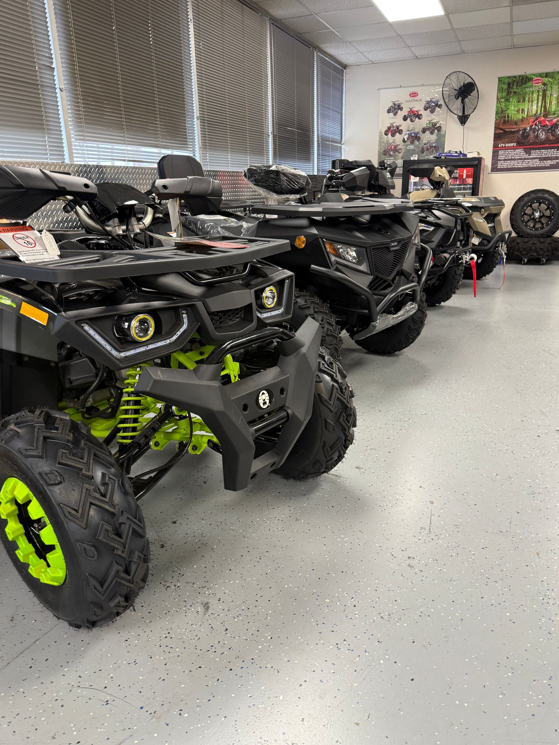 Row of parked black and neon green ATVs in a garage or showroom.