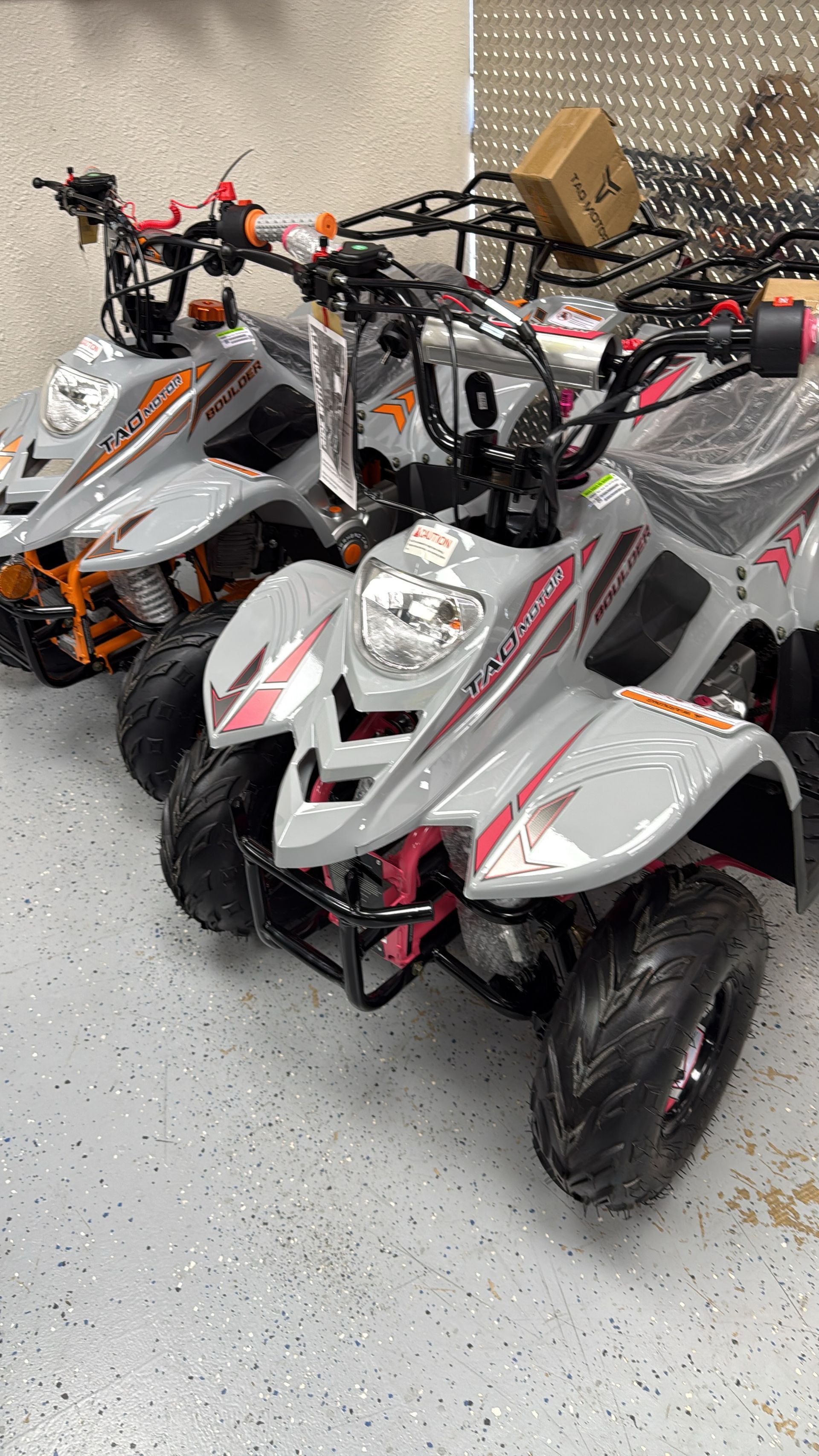 Three parked white and orange electric ATVs with red accents in a showroom or garage.