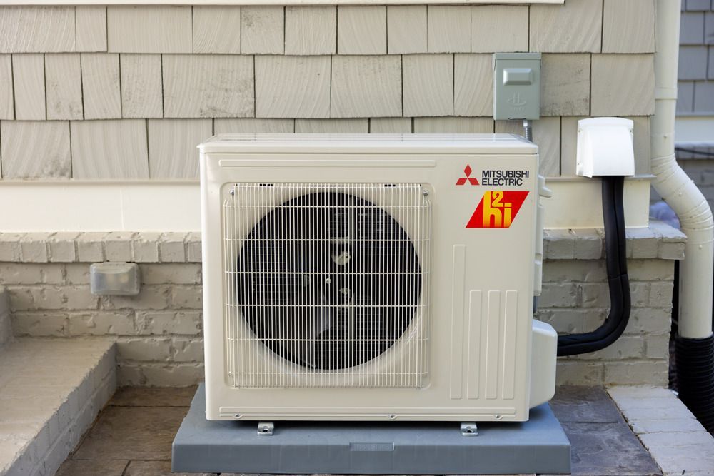 Outdoor Mitsubishi mini-split air conditioner unit beside a house wall on a concrete pad
