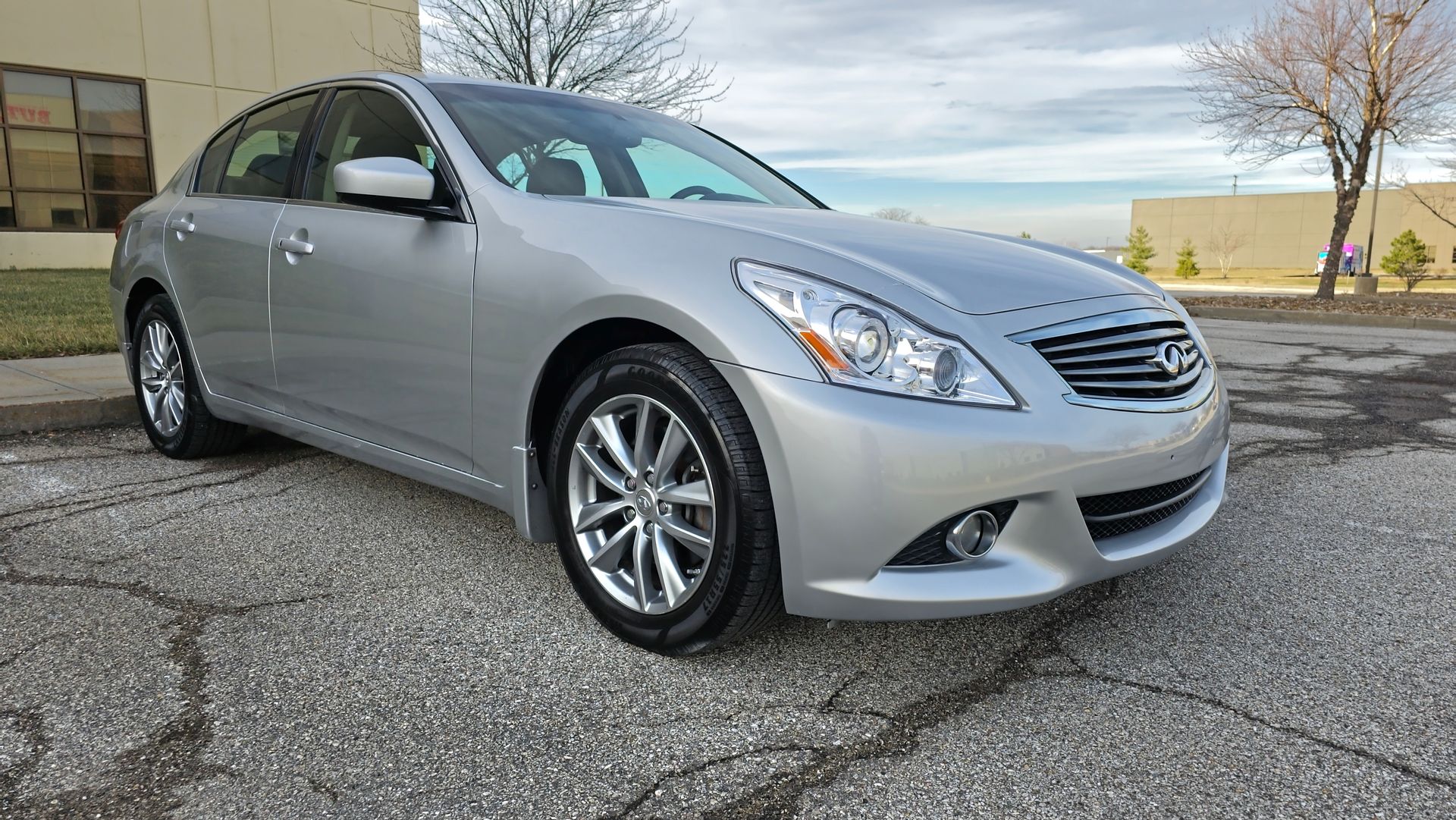 Silver Infiniti G37 sedan parked on cracked pavement, sunny day.