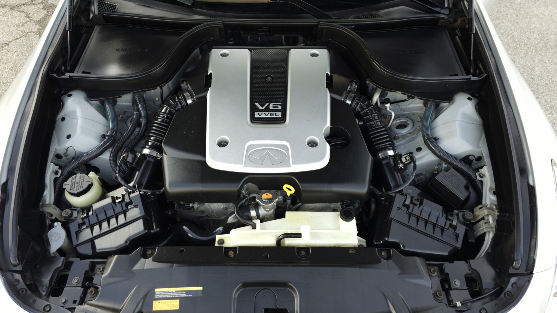 Car engine compartment showing a silver and black V6 engine, with white components on either side.