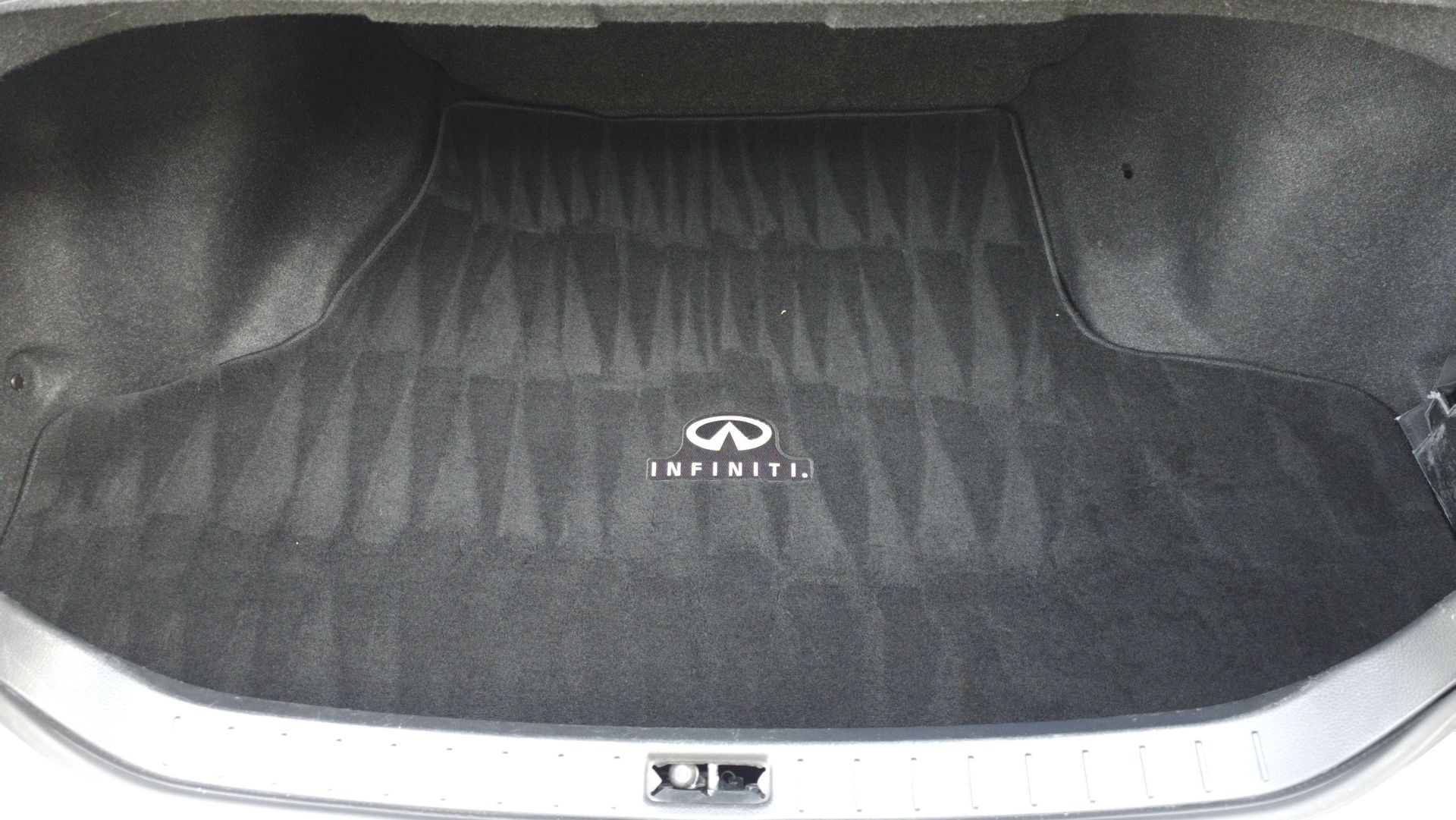 Car trunk with Infiniti logo on a black carpet mat.
