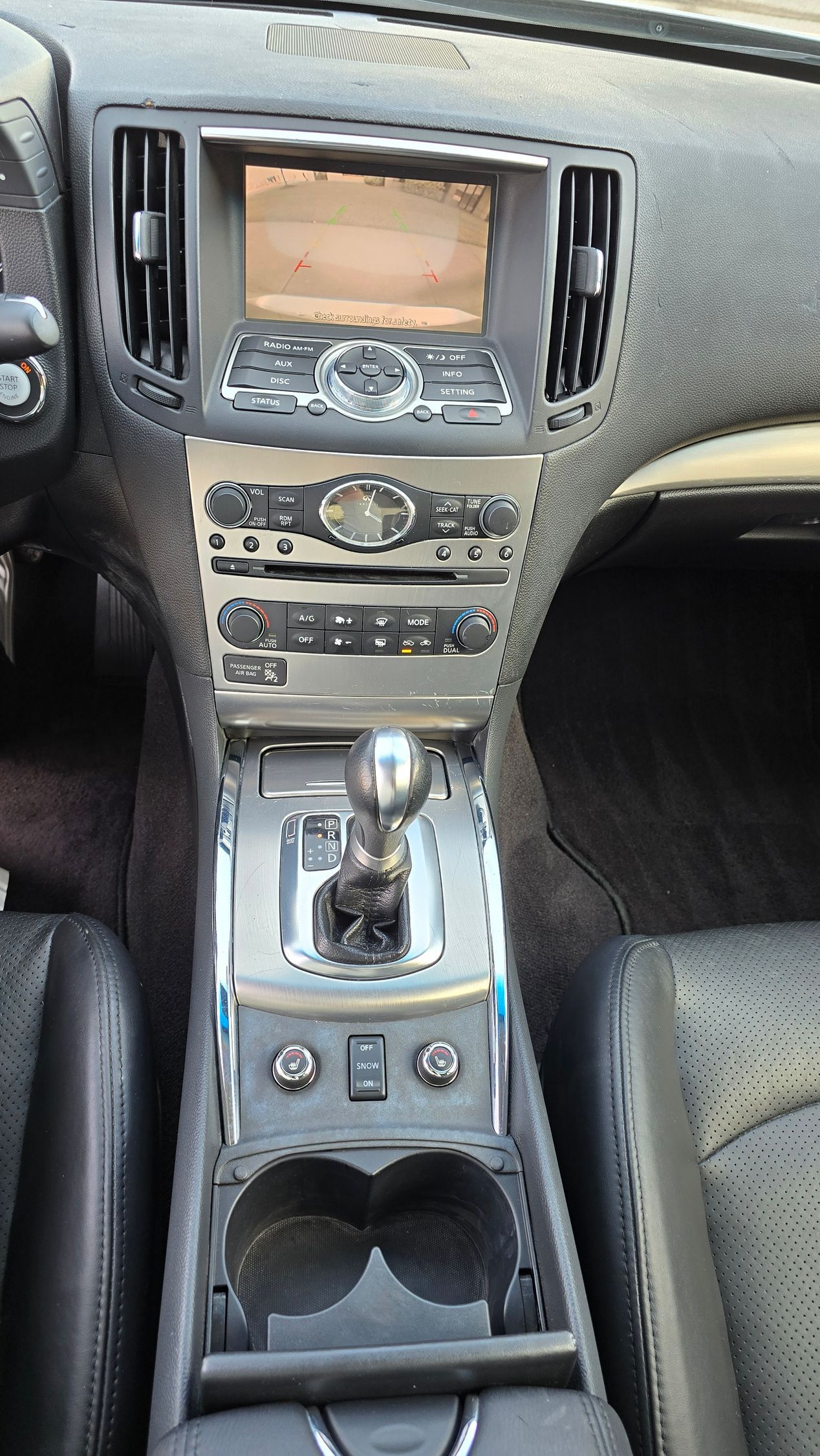 Car interior center console, silver and black, with gear shift, infotainment screen, and cup holders.