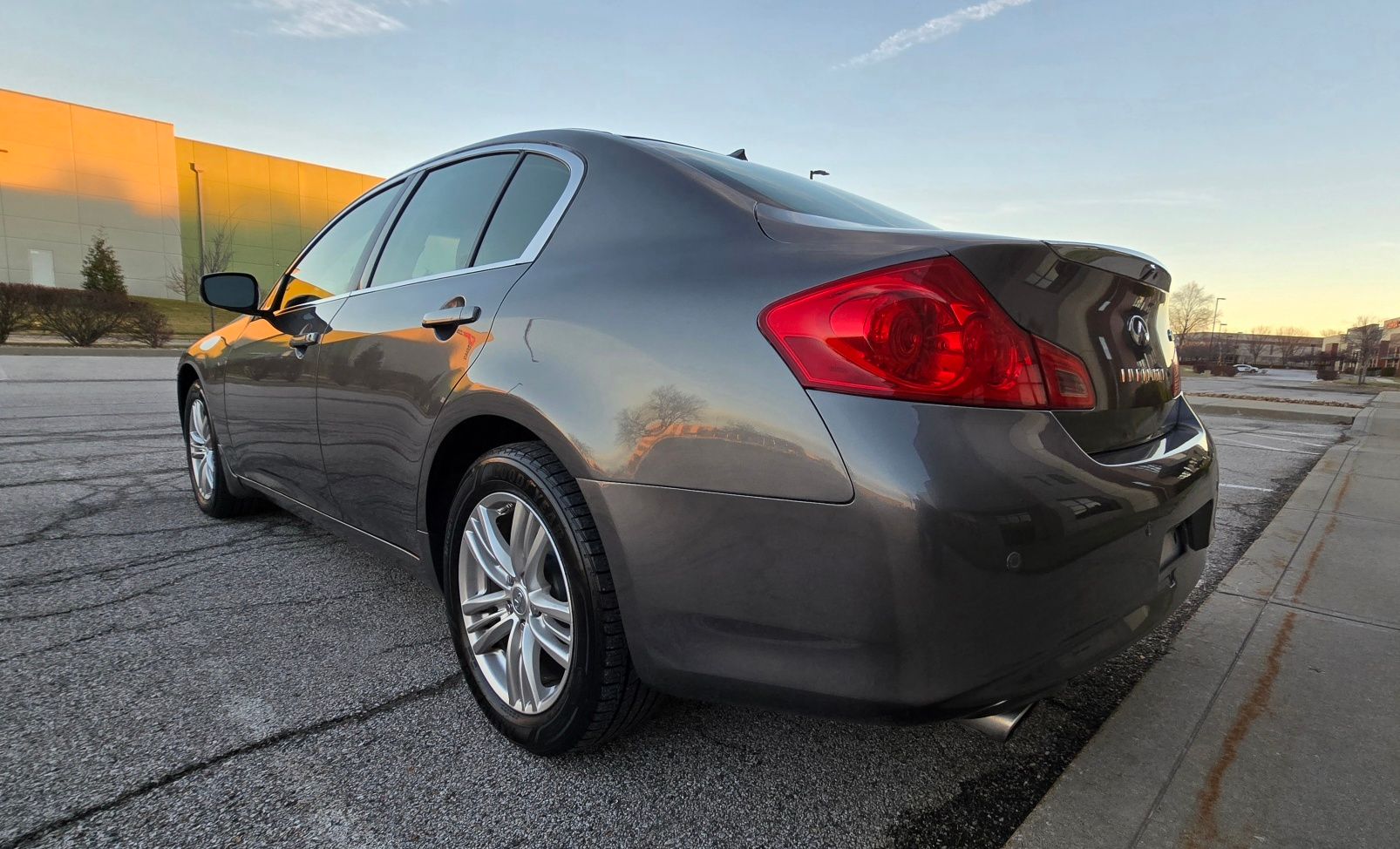 Gray Infiniti sedan parked on asphalt with the sun setting in the background.